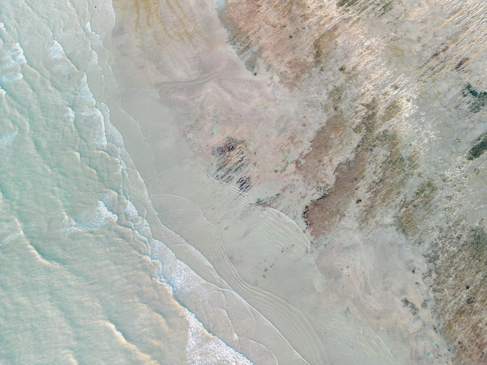 Aerial view of a beach where the turquoise ocean meets the sandy shoreline and rugged cliffs.