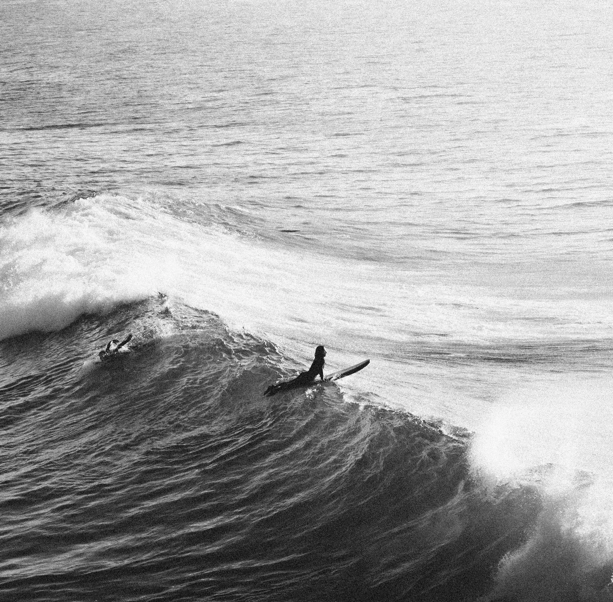 A person surfing on a wave in the ocean, captured in black and white.
