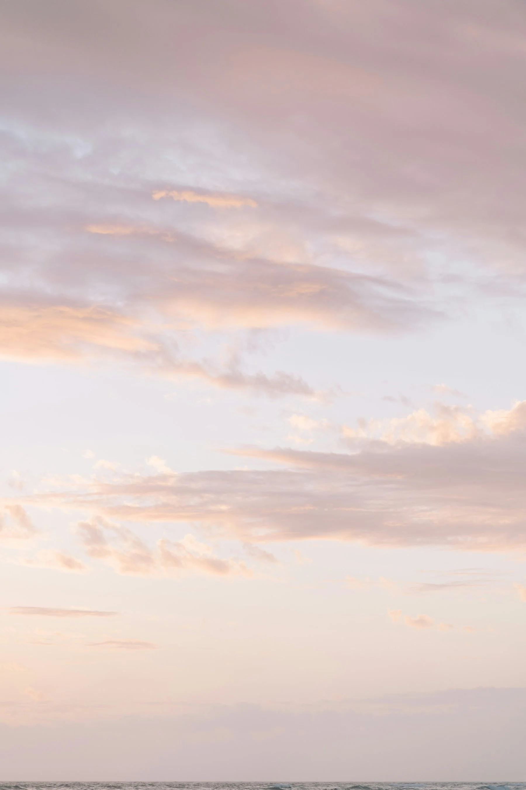 A pastel-colored sky with soft pink, purple, and orange clouds above a calm ocean horizon.
