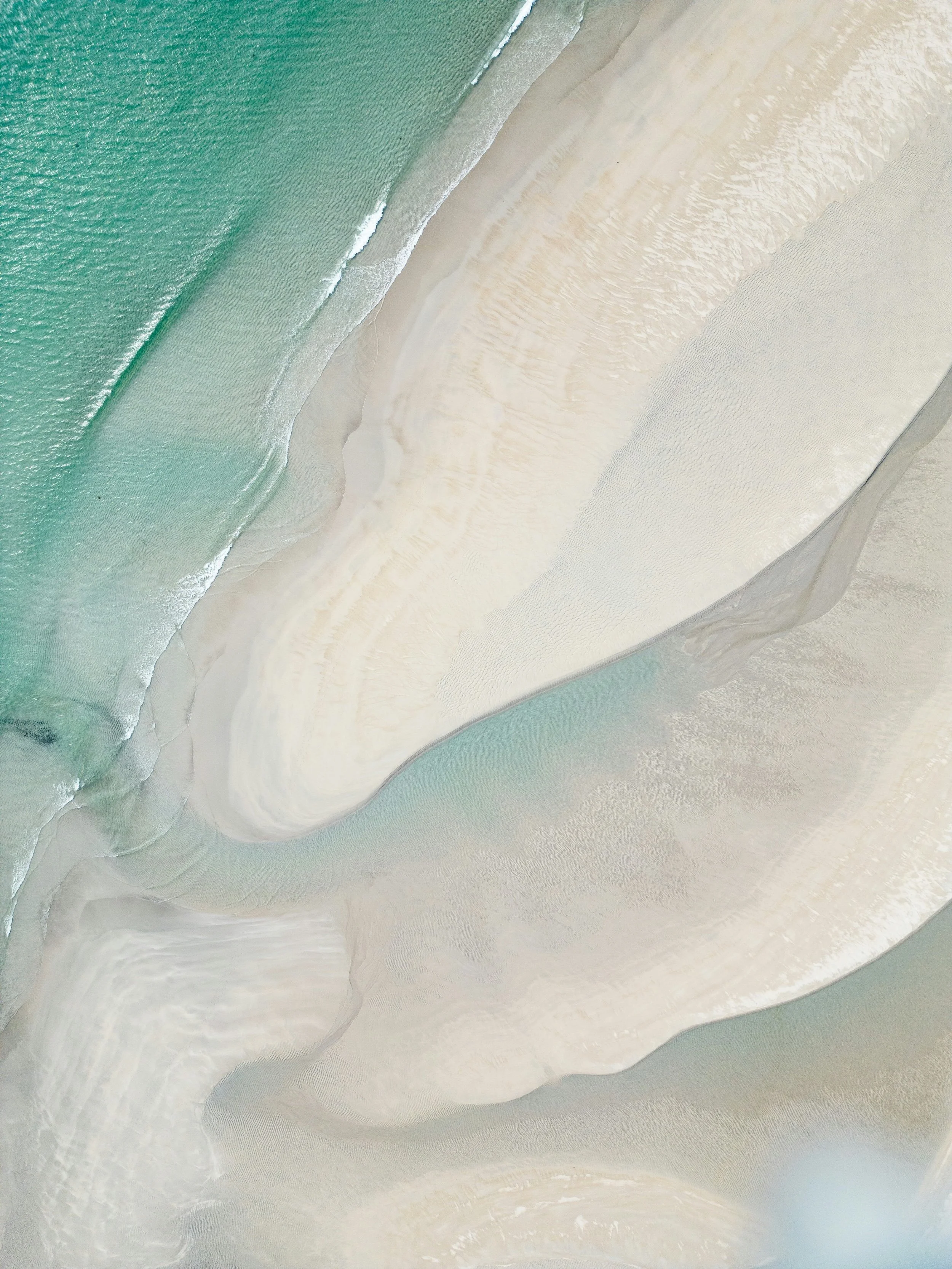 Aerial view of a beach with turquoise water, white sand, and gentle waves.