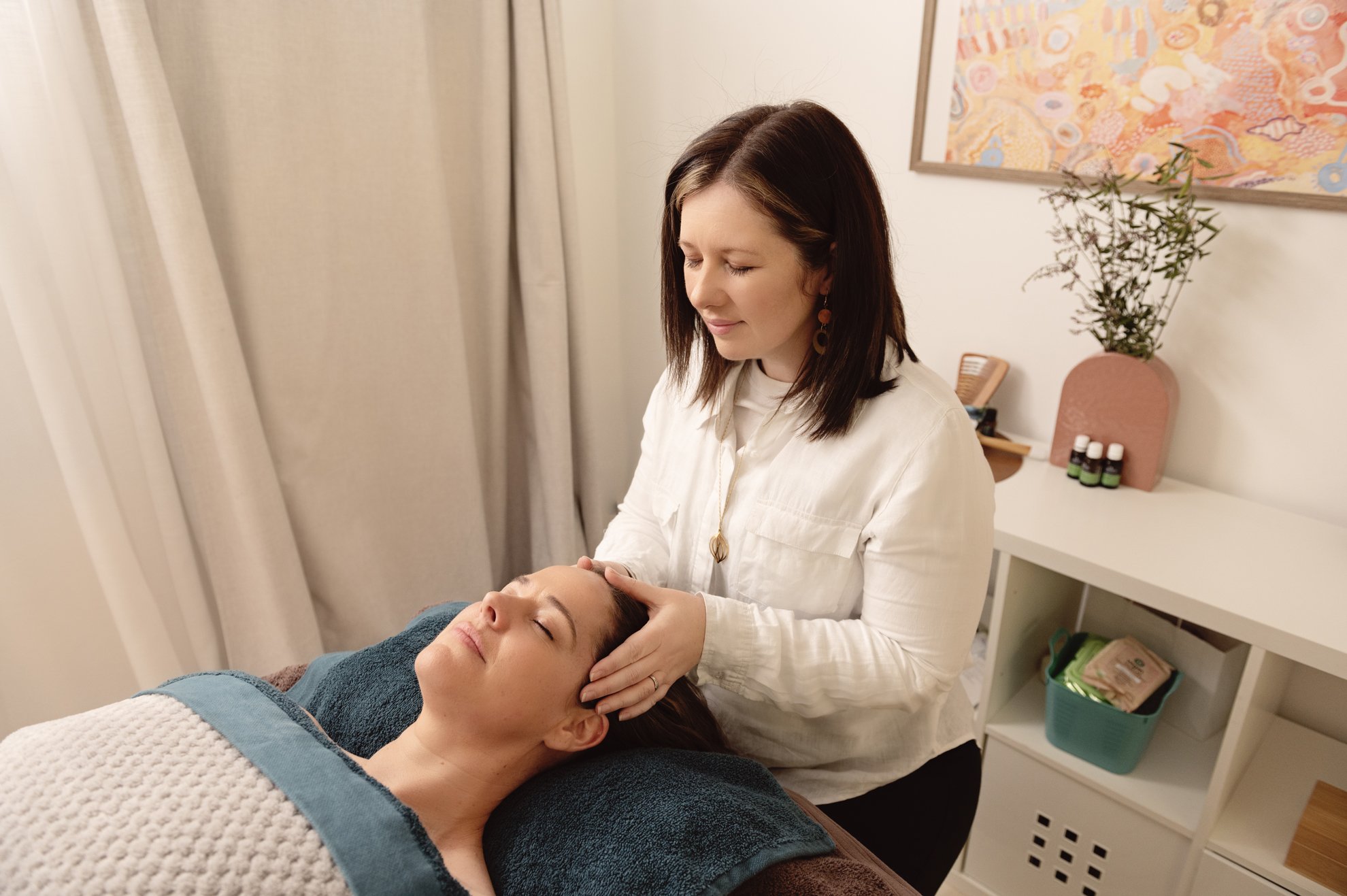 A woman receiving a facial or head massage from a massage therapist in a spa or treatment room.