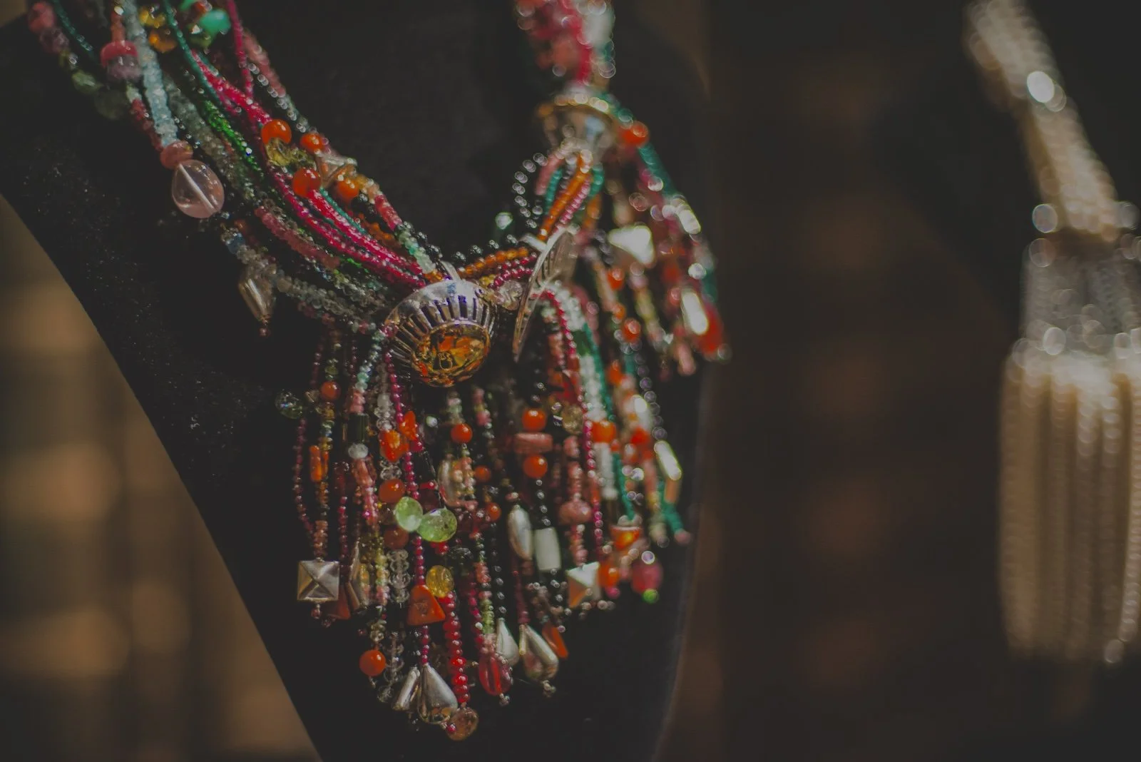 Close-up of colorful beaded necklaces with various shapes hanging on a black display bust.