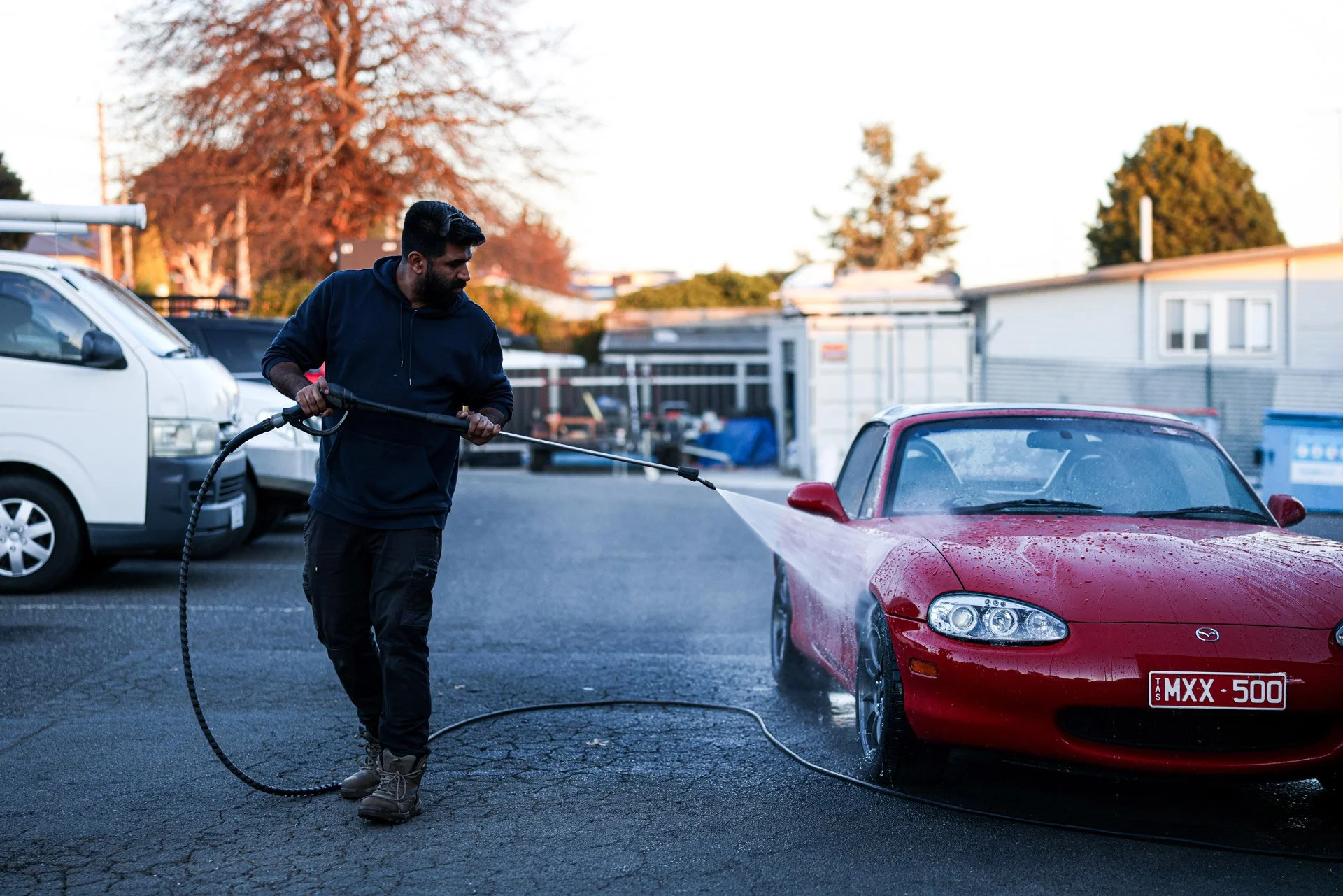 Man washing a red sports car with a hose in a parking lot