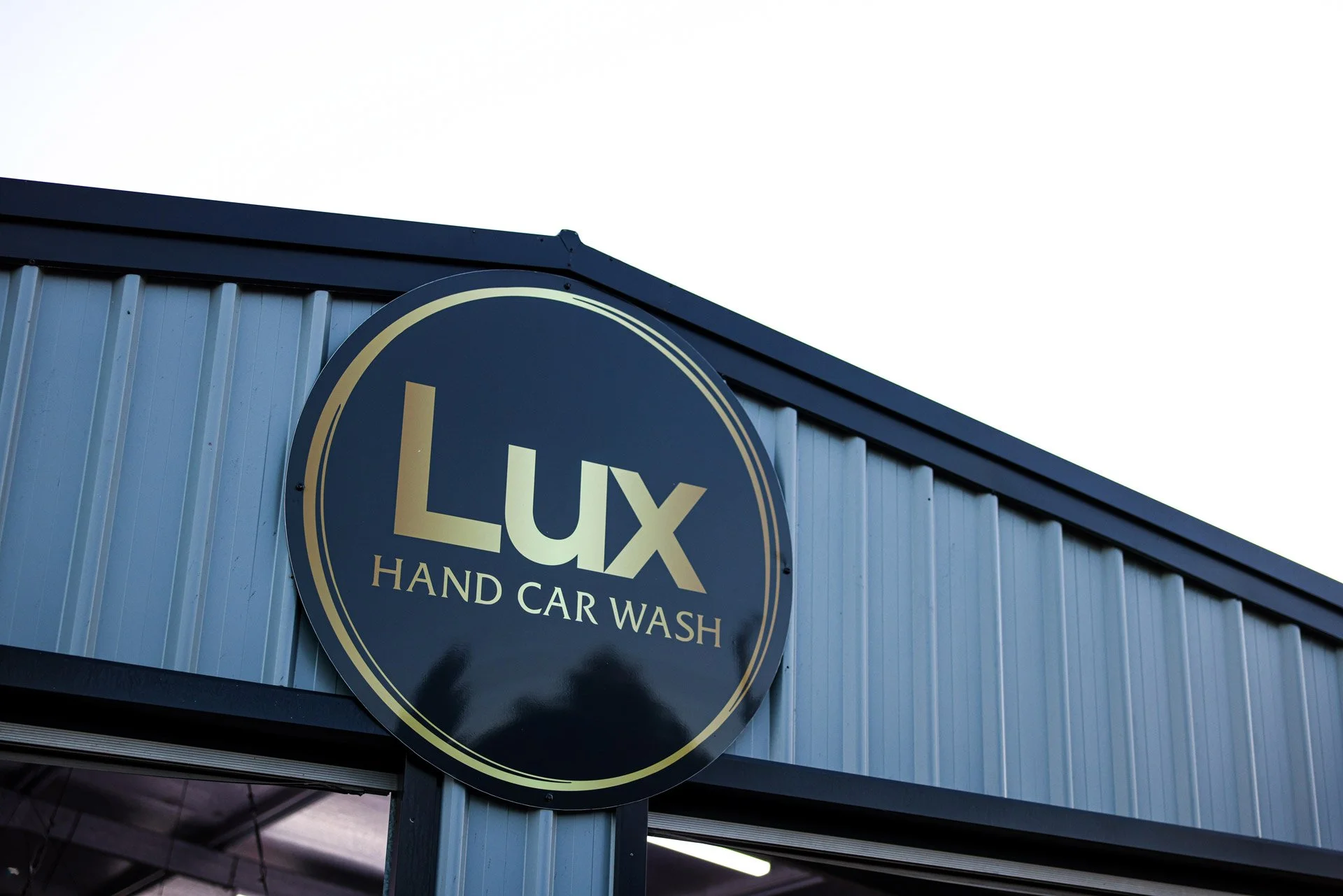 Exterior view of a building with a round sign that reads "LUX HAND CAR WASH" in gold and white lettering on a dark background