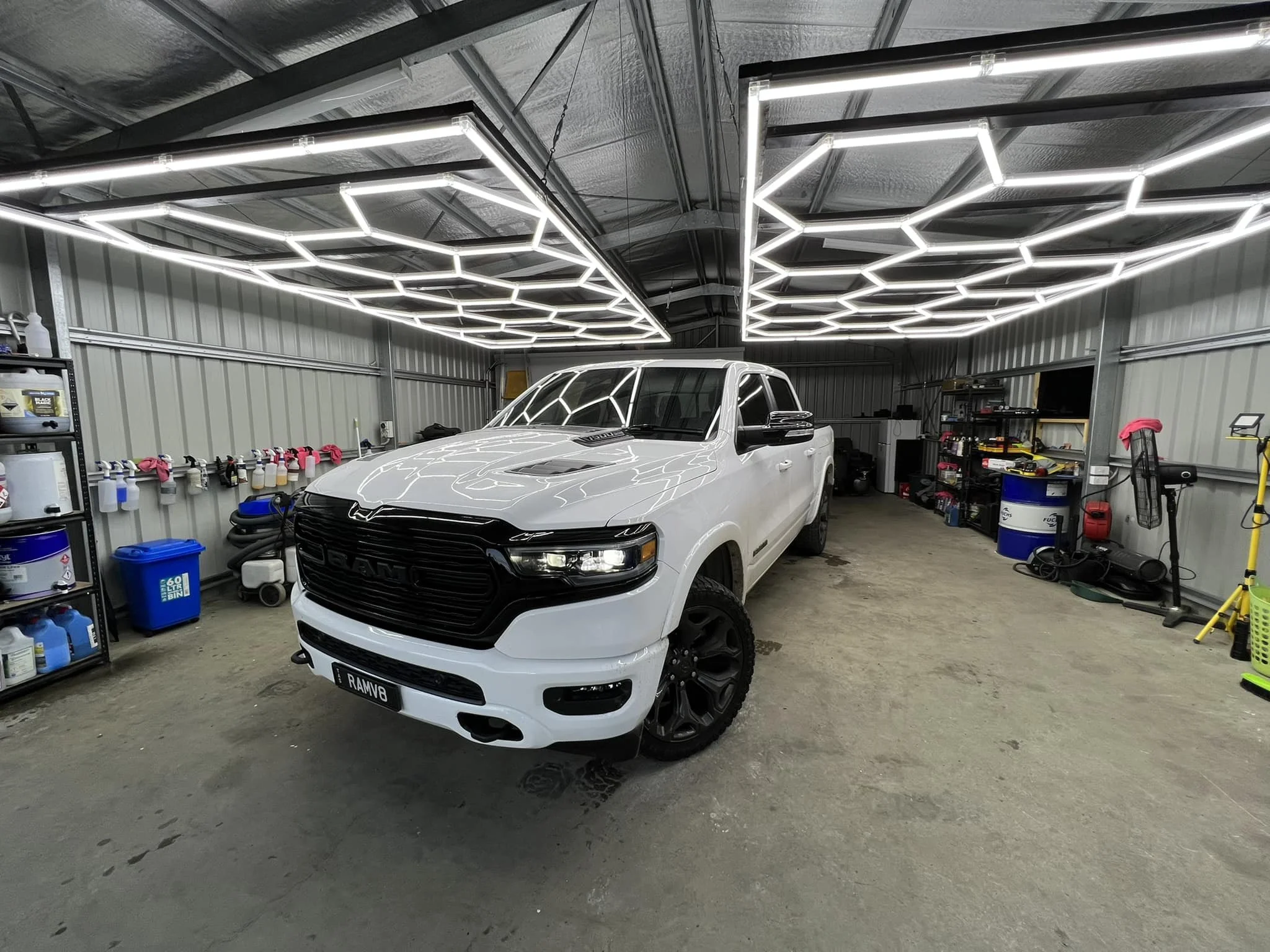 White pickup truck with black grille inside a well-lit garage with shelves and tools.