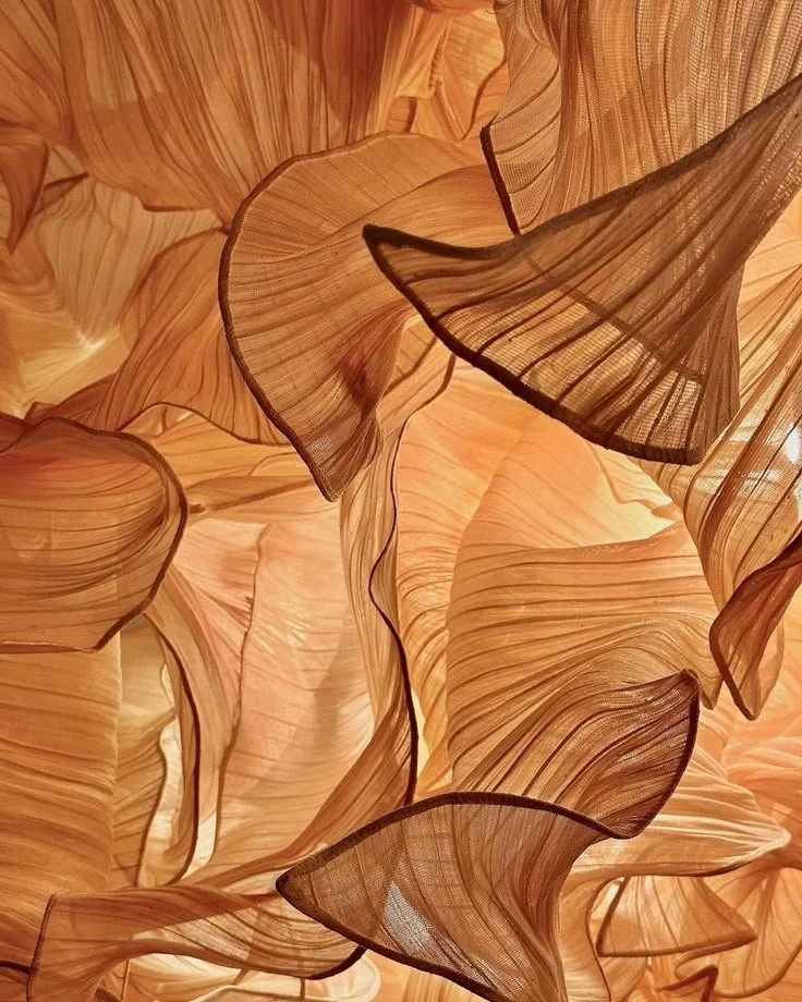 Close-up of a decorative light fixture resembling flowing, curved fabric or leaves with warm, amber tones.