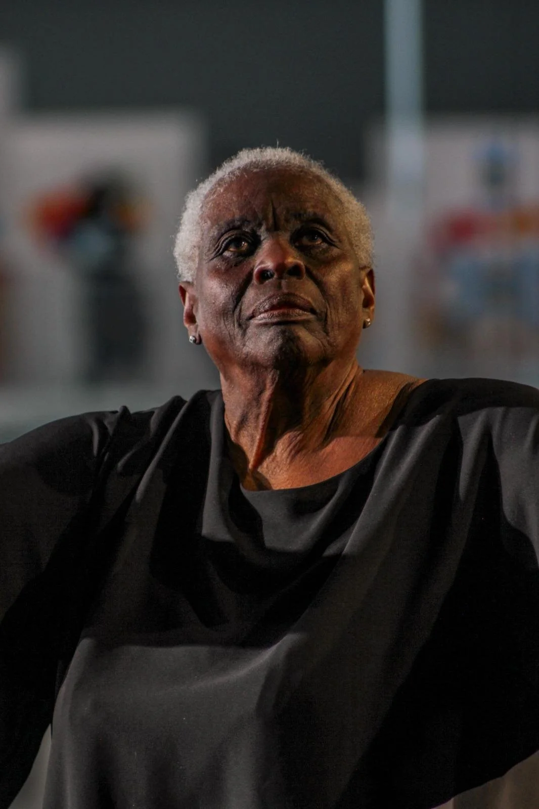 Portrait d'Elsa Wolliaston. Portrait d'une femme âgée avec des cheveux gris, portant un haut noir, expression sérieuse et regardant légèrement vers le haut.