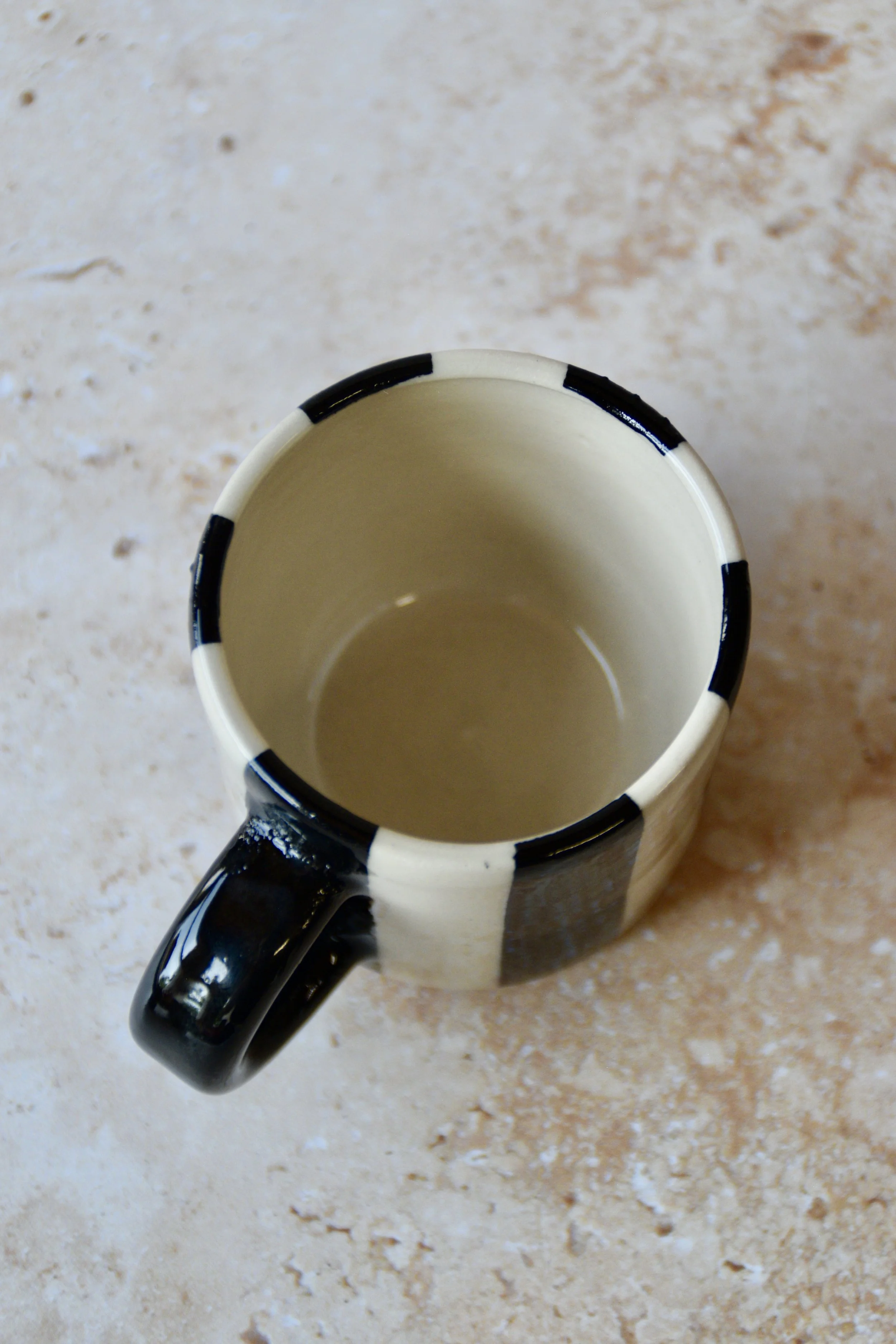 A ceramic mug with a cream interior and exterior. The exterior has alternating black and cream vertical stripes. The handle is solid black. The mug is designed for hot drinks.