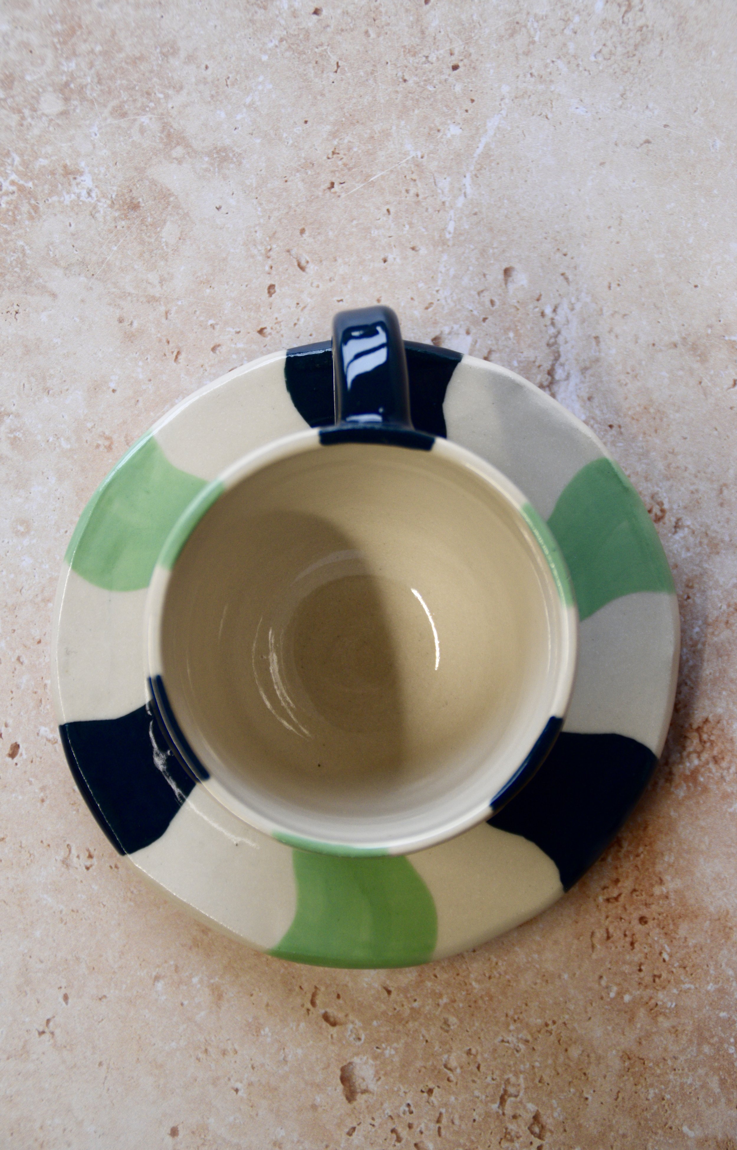 Top view of a handmade ceramic espresso cup and saucer featuring a wavy stripe pattern in dark green and matcha tones on a cream base.