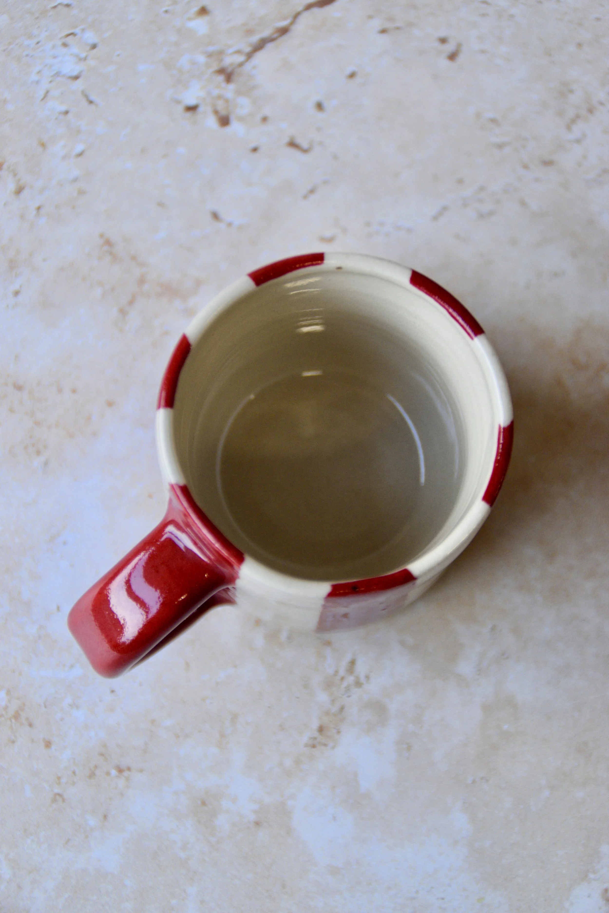 Top view of small handmade ceramic espresso cup with glossy interior and red striped rim, shown empty.