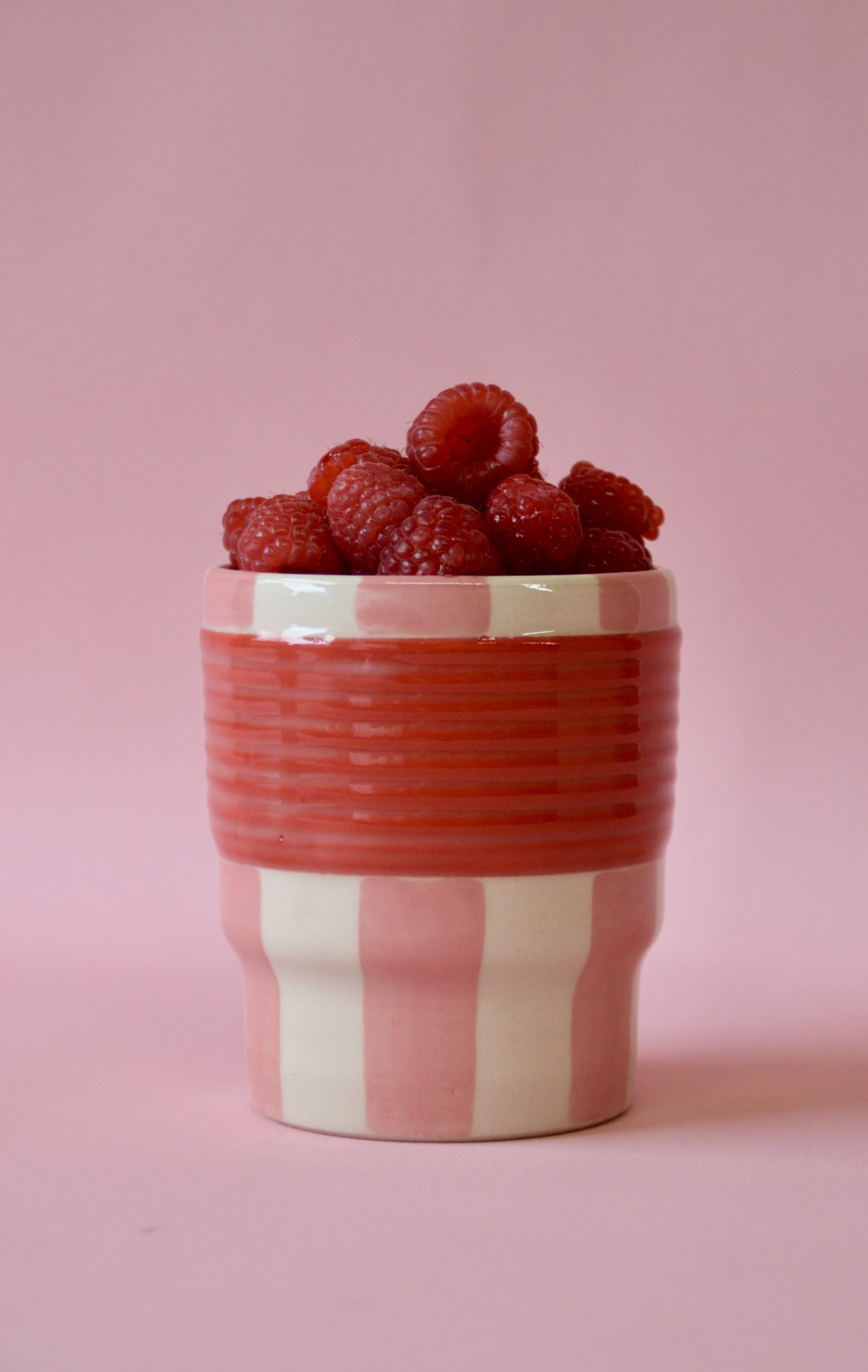 Pink and red striped ceramic tumbler with raspberries