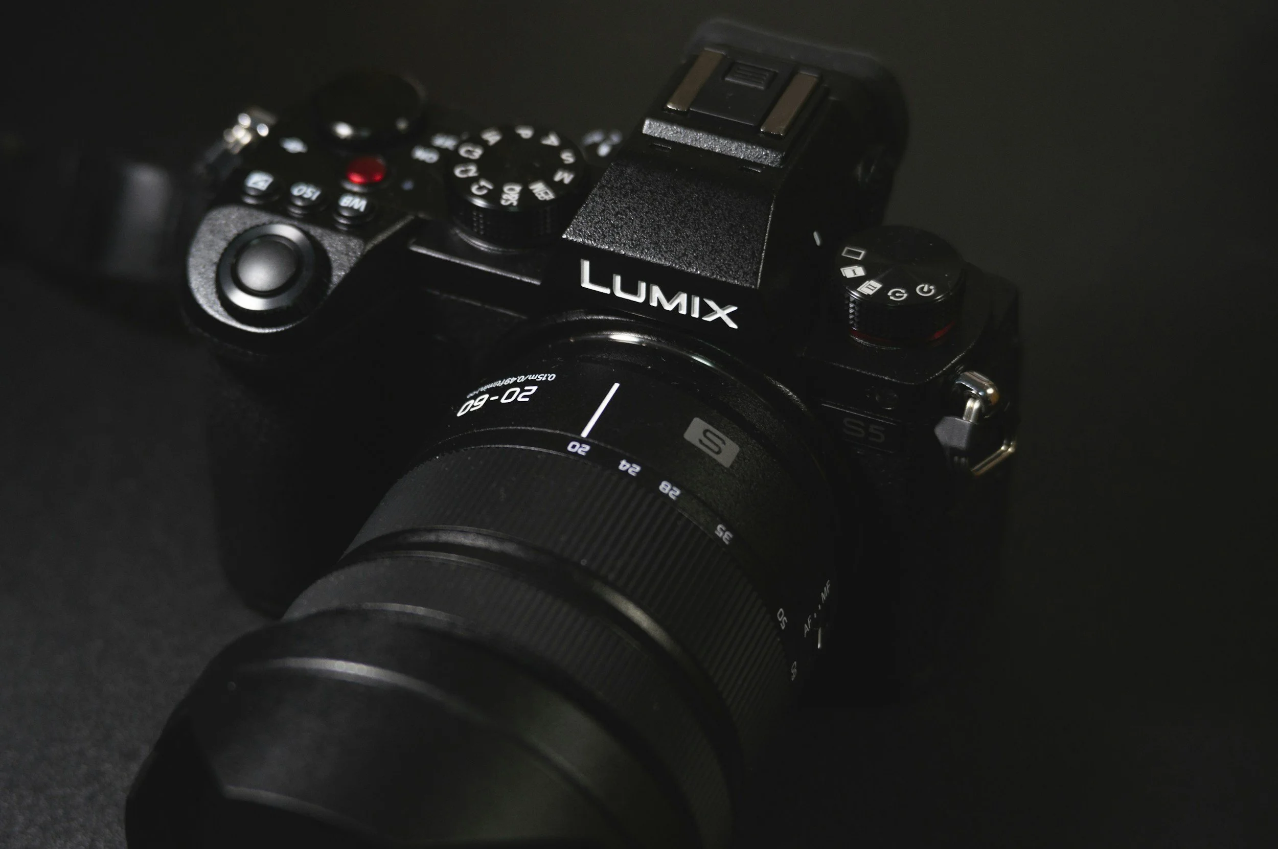 Digitale Spiegelreflexkamera der Marke Lumix mit großen Objektiv, auf dunklem Hintergrund liegend.