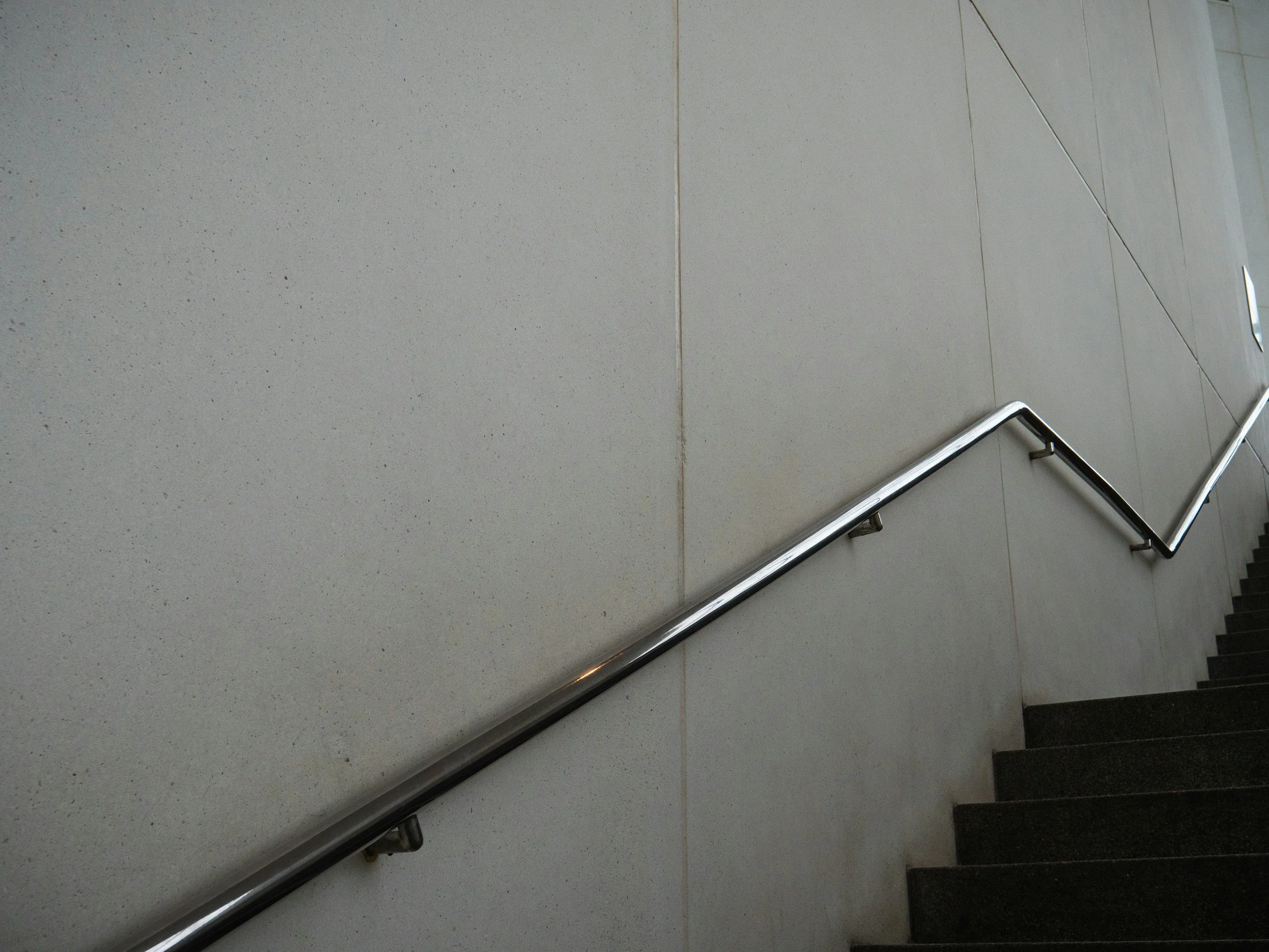 A staircase with dark steps and a metal handrail along a light-colored wall.