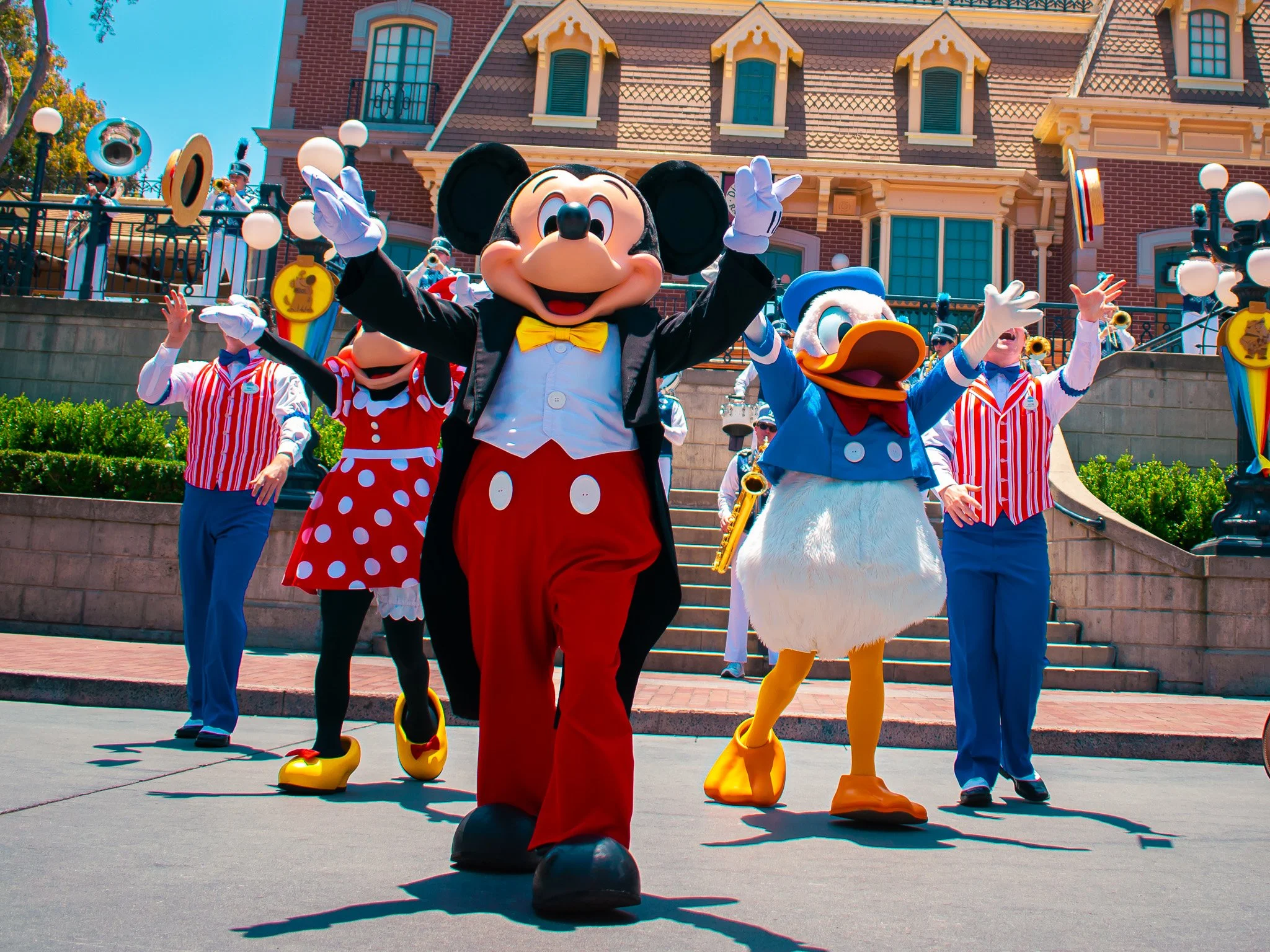Mickey Mouse, Donald Duck, and other characters performing during a parade at Disneyland with a castle in the background.