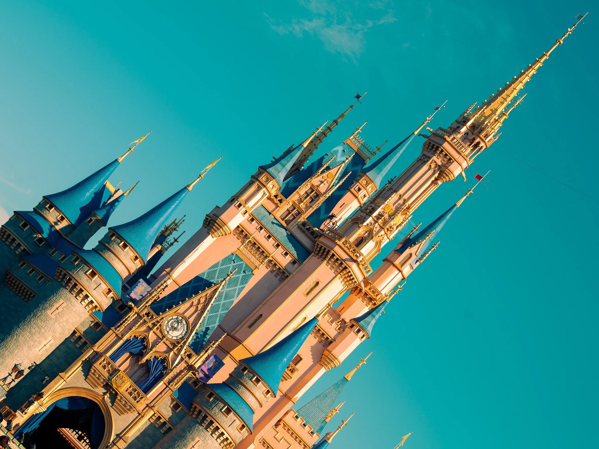 The Disney castle at Walt Disney World with pink towers and blue spires against a clear blue sky.
