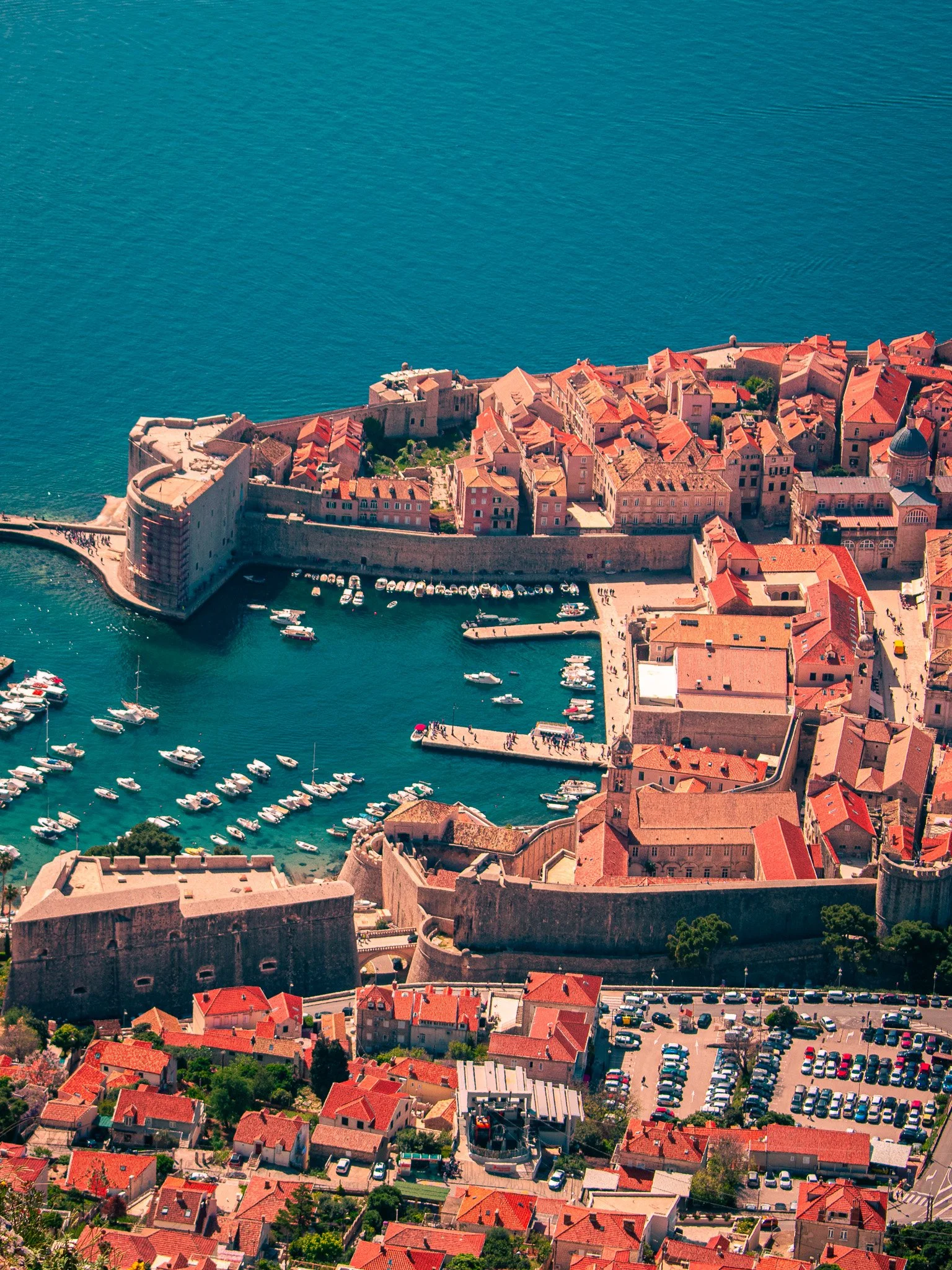 Aerial view of Dubrovnik, Croatia with ancient stone walls, red-tiled roofs, and a harbor filled with boats.