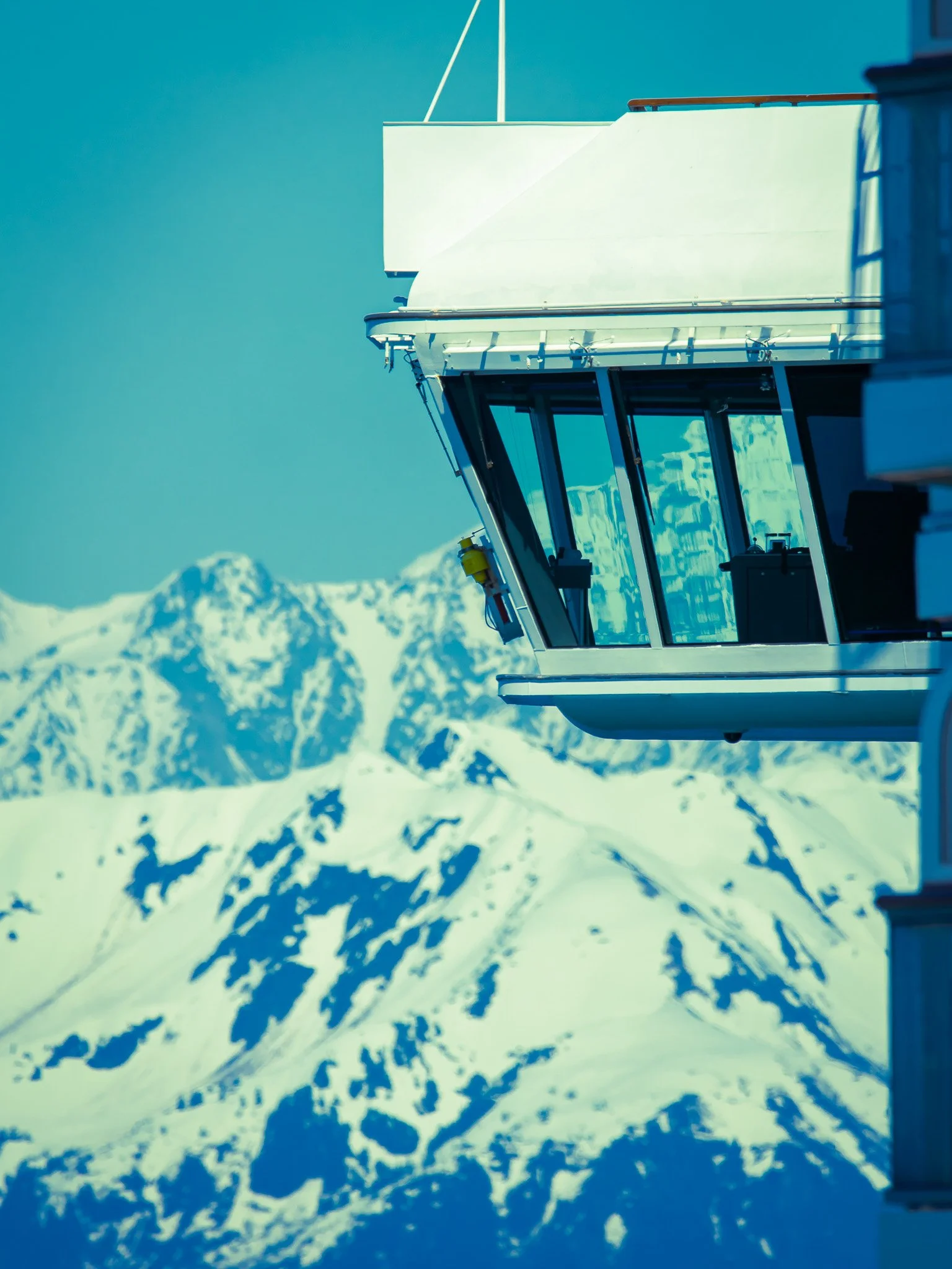 Close-up of a ski lift station overlooking snow-covered mountain peaks.