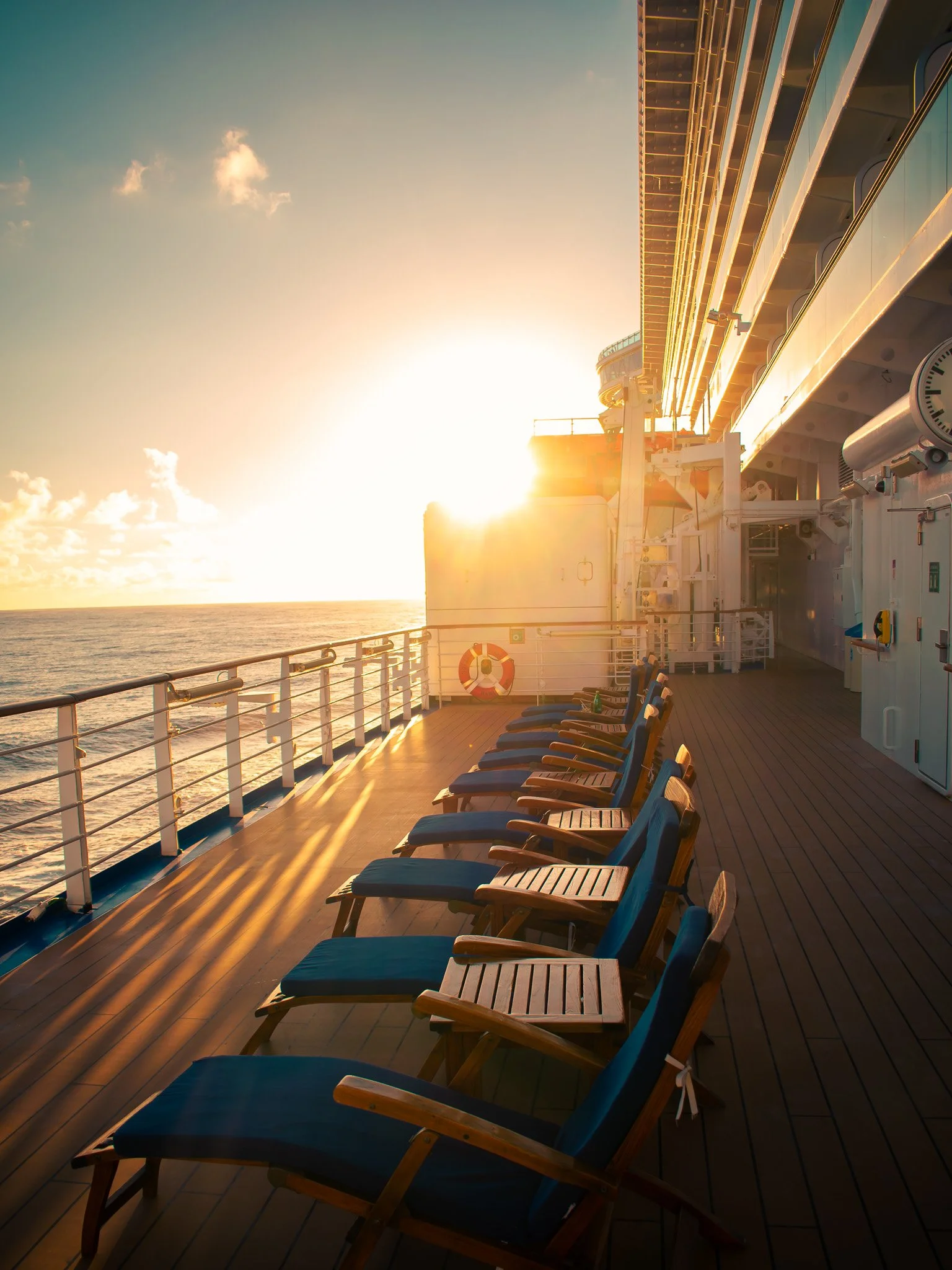Rows of chairs on the deck of a cruise ship with the sun setting over the ocean.