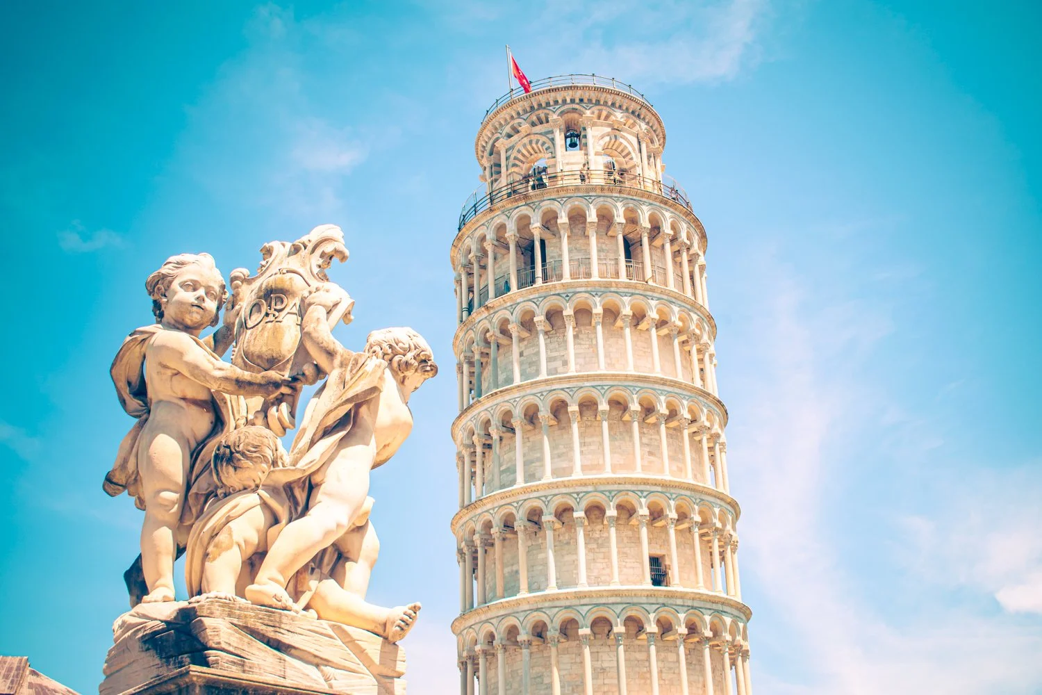 Stone sculpture of children and animals with the Leaning Tower of Pisa in the background against a blue sky.