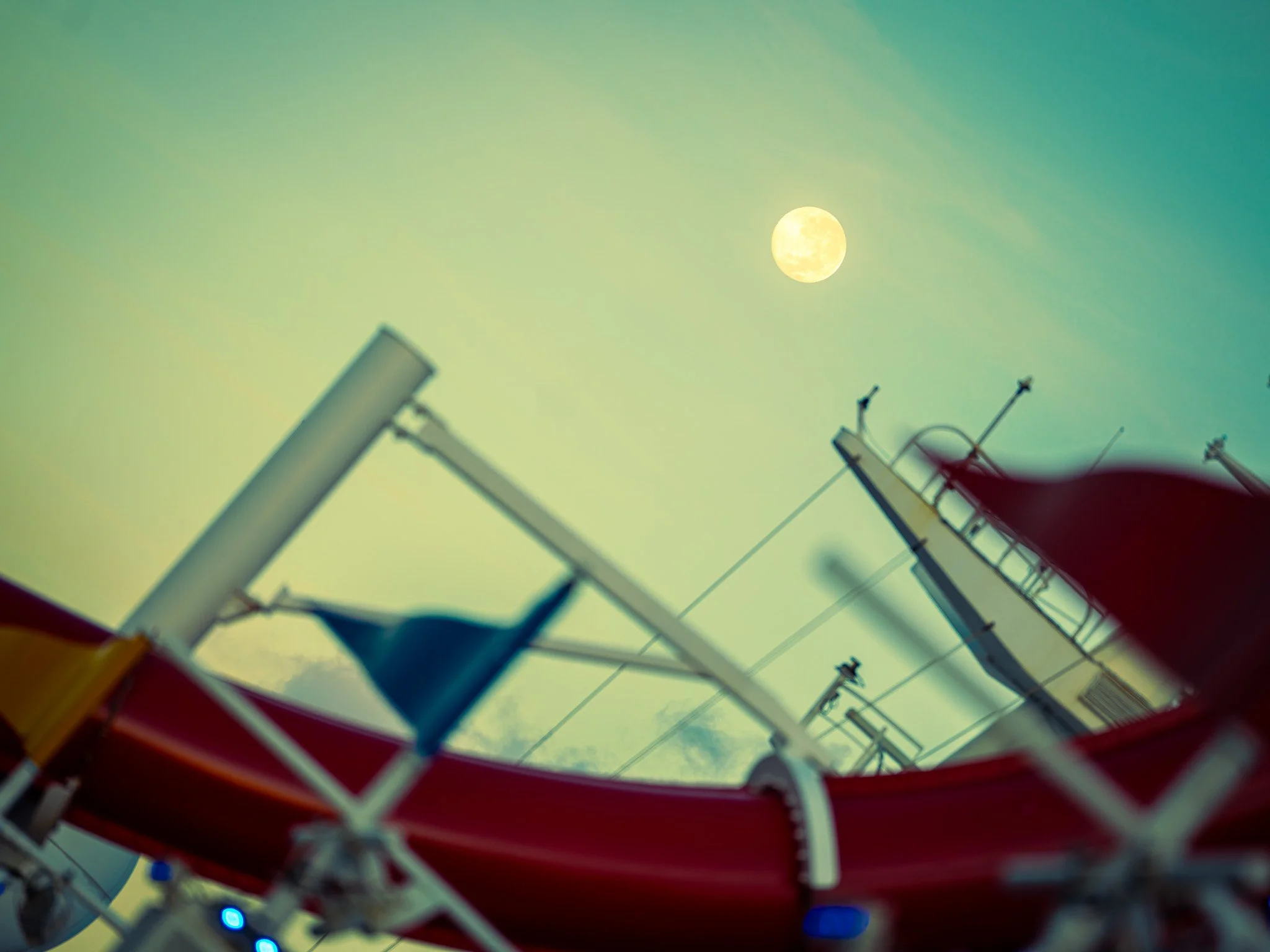 View of a moon in the sky with blurred foreground featuring a parasail and parts of a parasailing boat or equipment.