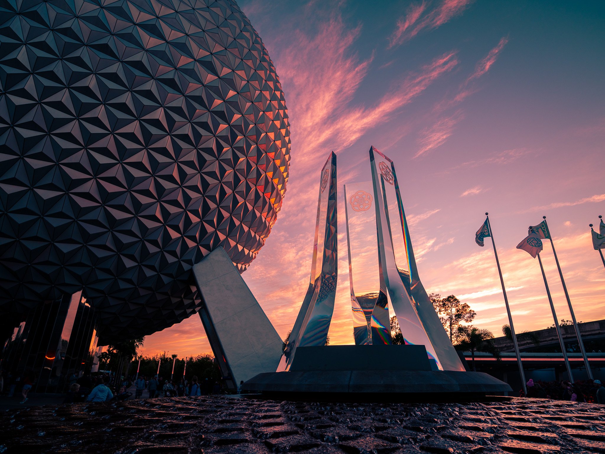 EPCOT theme park at sunset with the geodesic sphere and monument sculptures, and flags in the background.