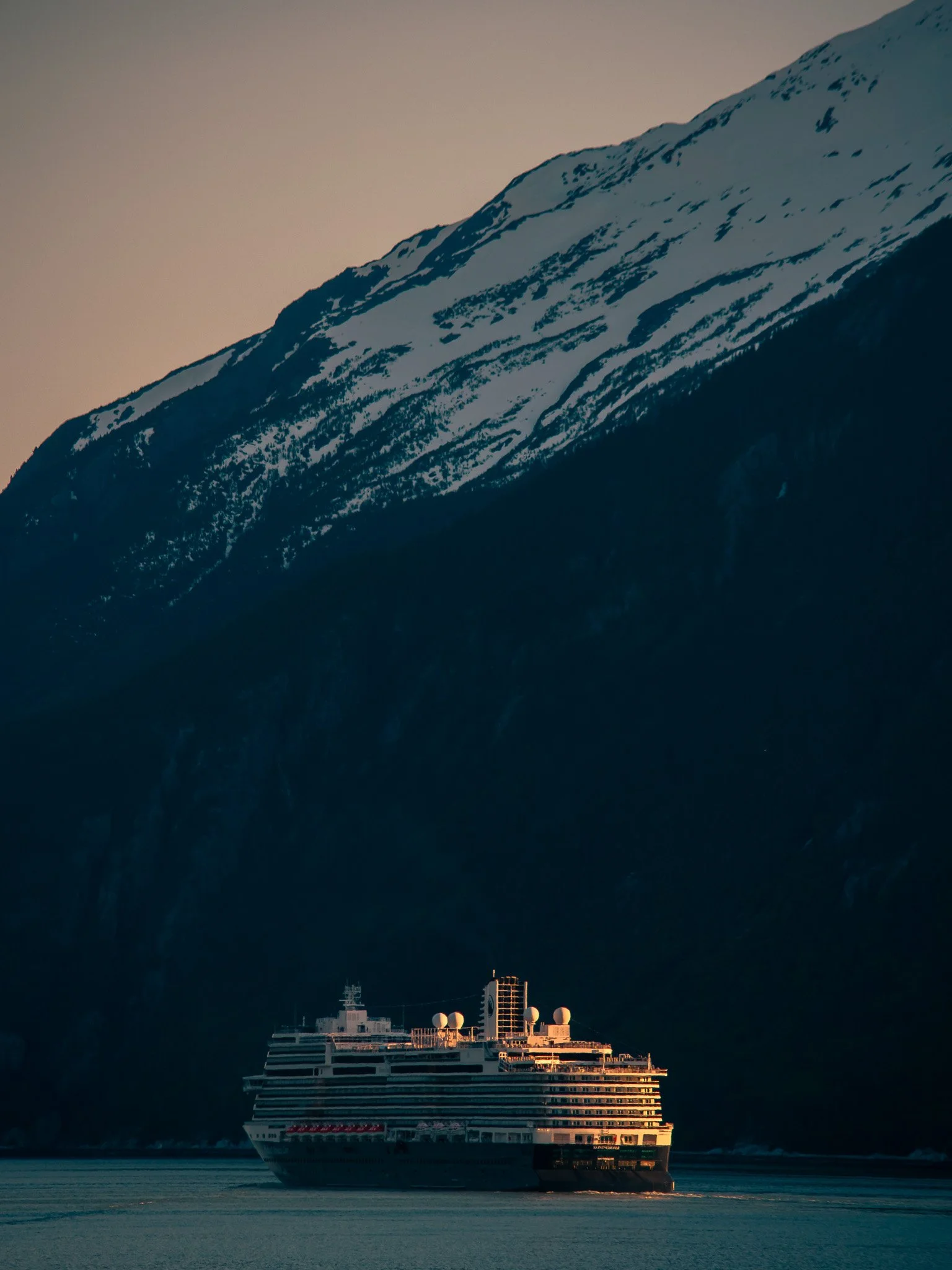 A cruise ship sailing in a body of water with a mountain range in the background.