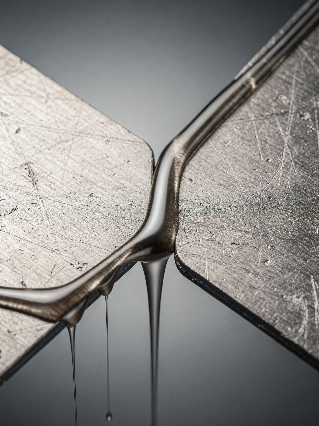 Close-up view of two metal surfaces joined with rivets, with liquid metal or lubricant dripping from the joint.