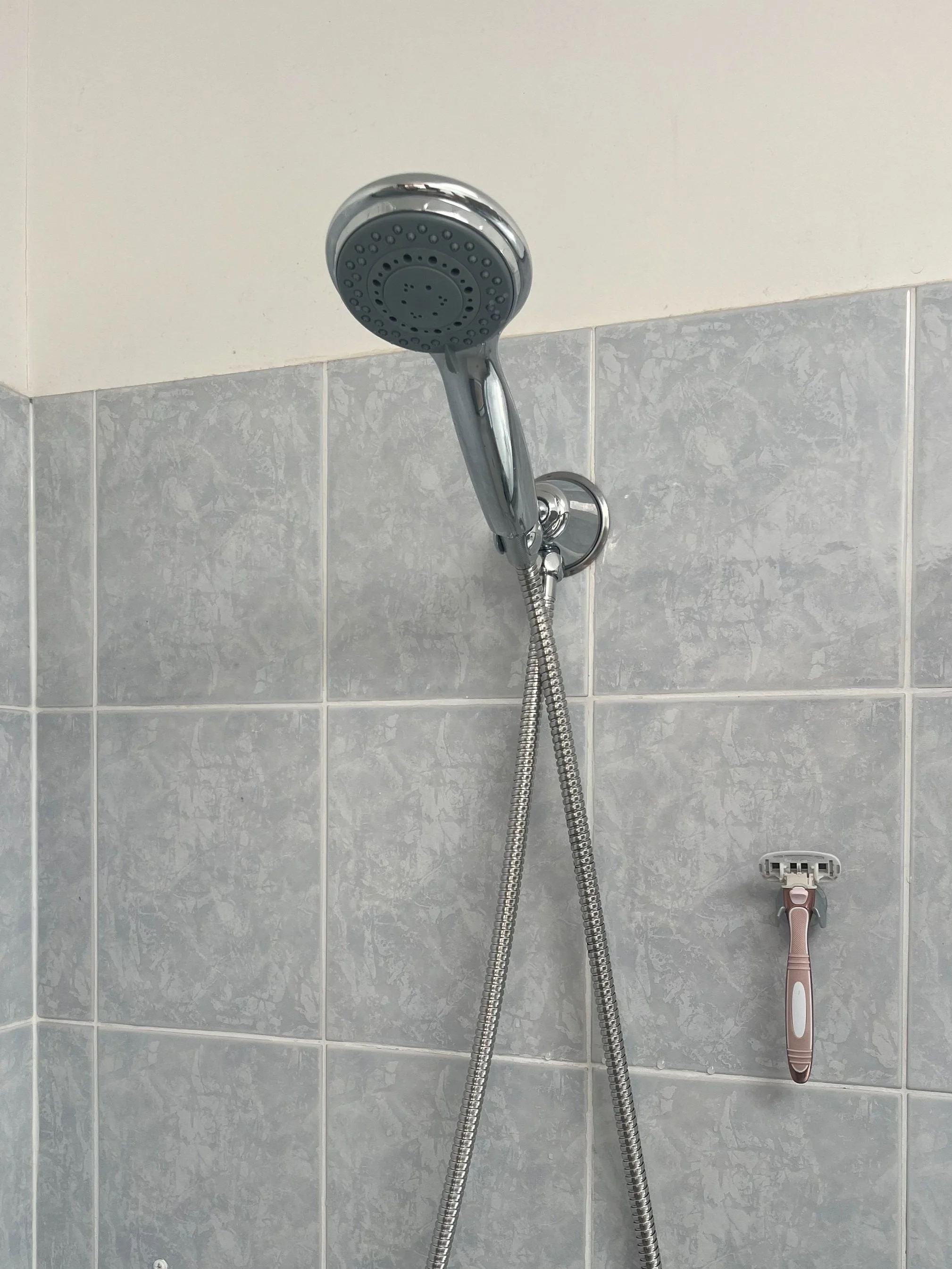 Showerhead mounted on a tiled bathroom wall with a razor hanging nearby.