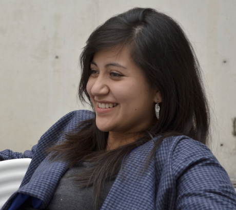 Woman with long dark hair smiling and wearing a blue checkered blazer.