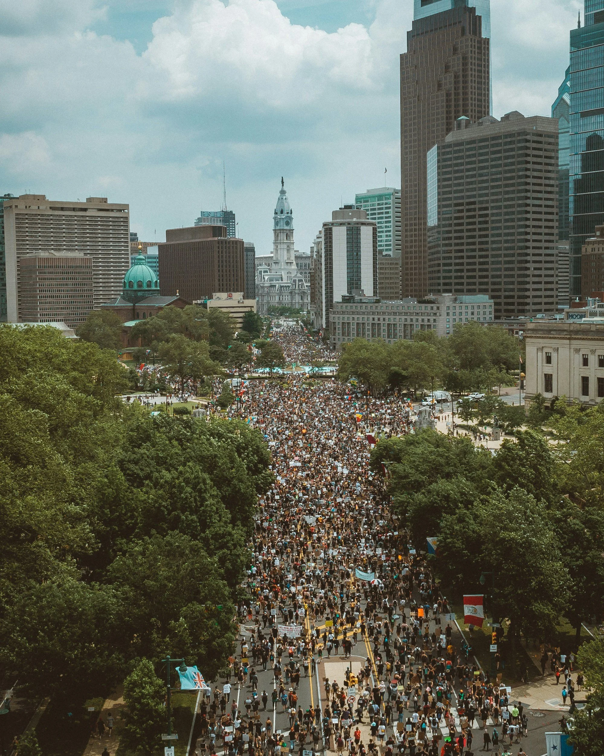 A large crowd of protesters fills a city street, surrounded by tall buildings and trees, with a cloudy sky overhead. Another Good Day Maxine Hassing Impact Businesses Grow and Build Your Business. We are a Strategy and Marketing Agency Entrepreneurs