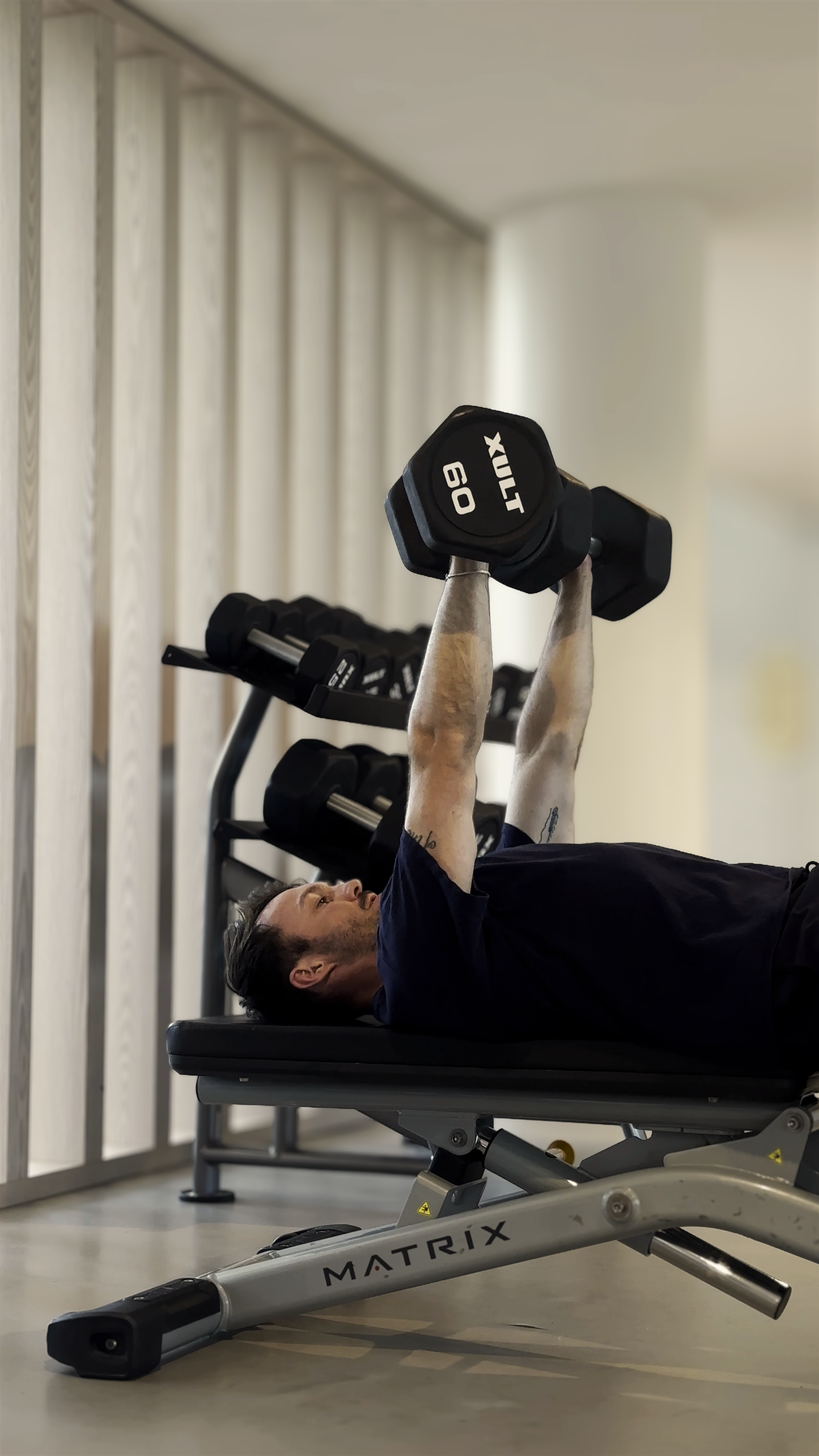 A man lying on a workout bench, lifting a dumbbell with both arms