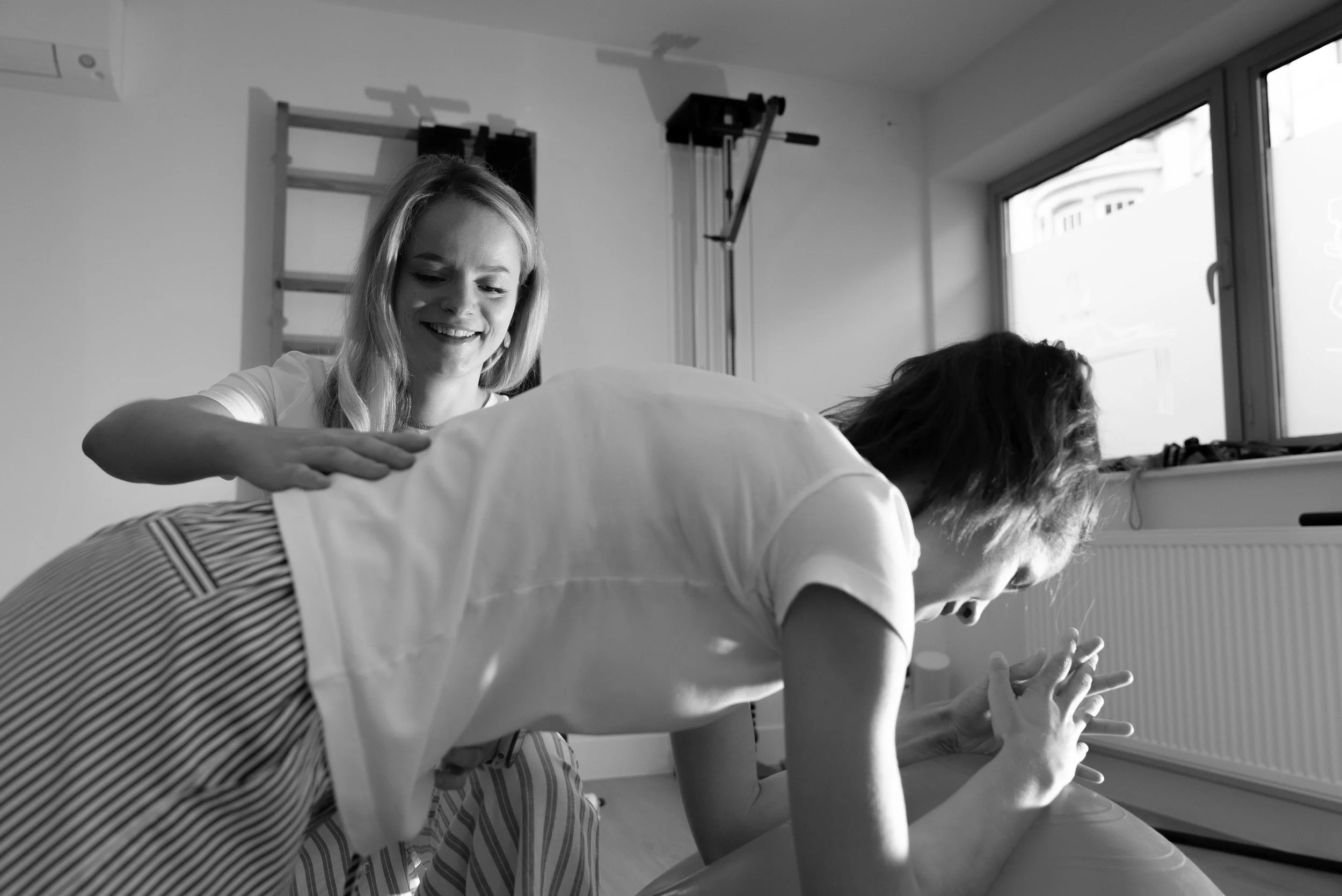 Twee vrouwen die yoga doen, één ondersteunt de ander in een yoga houding in een sportschool, zwart-wit foto.