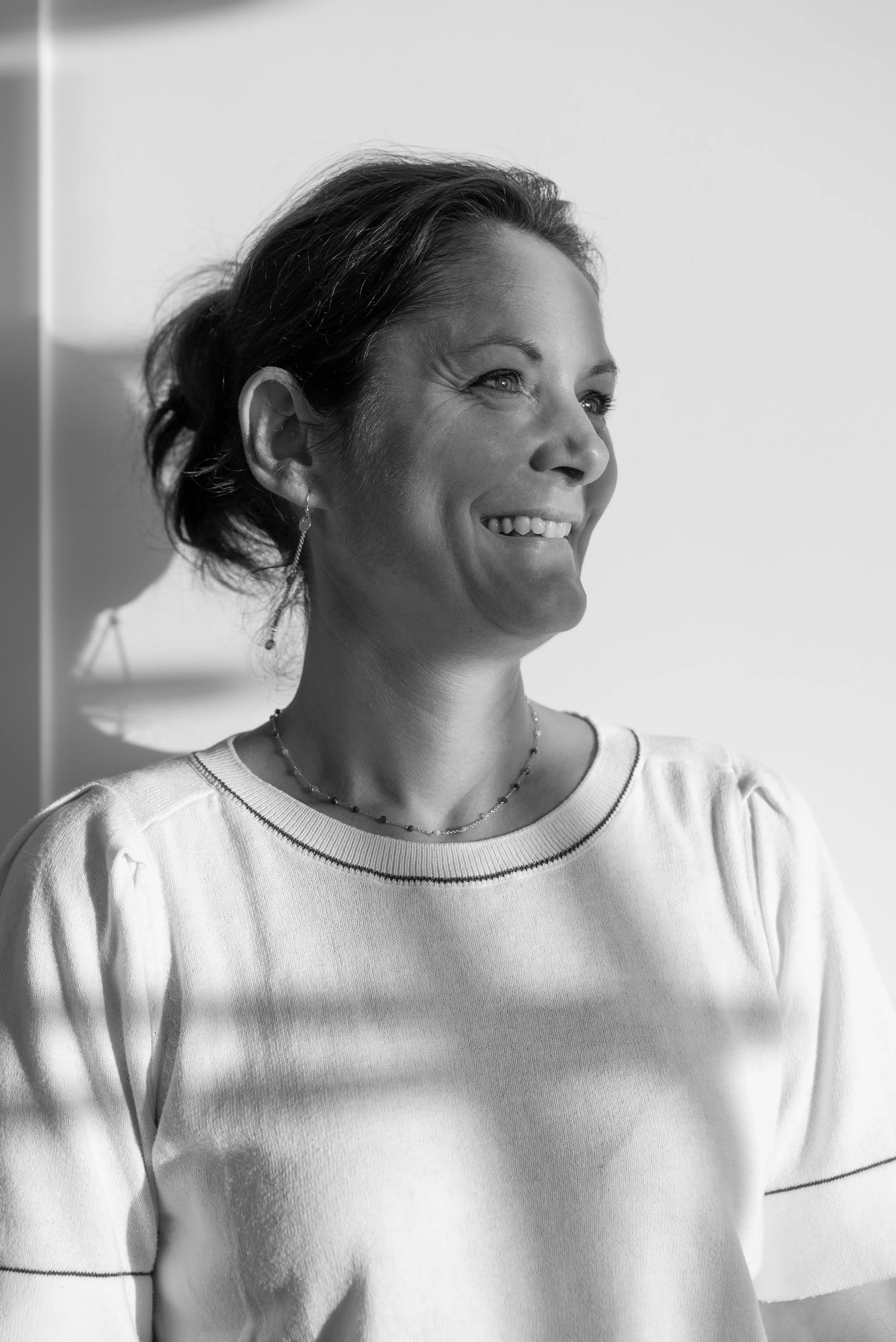 Portret van een lachende vrouw met korte haar, oorbellen en een ketting, in zwart-wit.