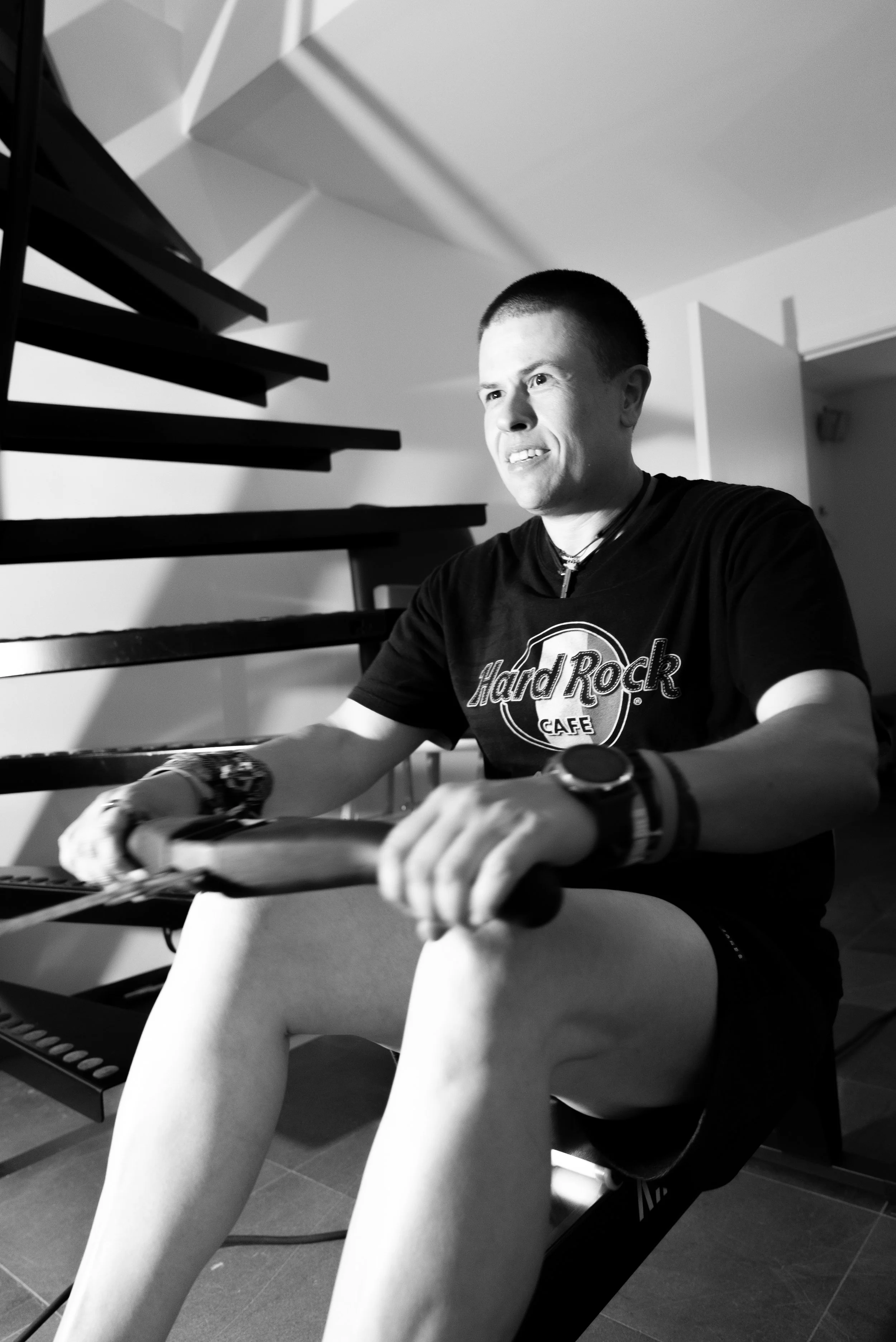 Man op een hometrainer, zwart-wit foto, Hard Rock Café shirt, vlakke vloer, binnenruimte, lage hoek.