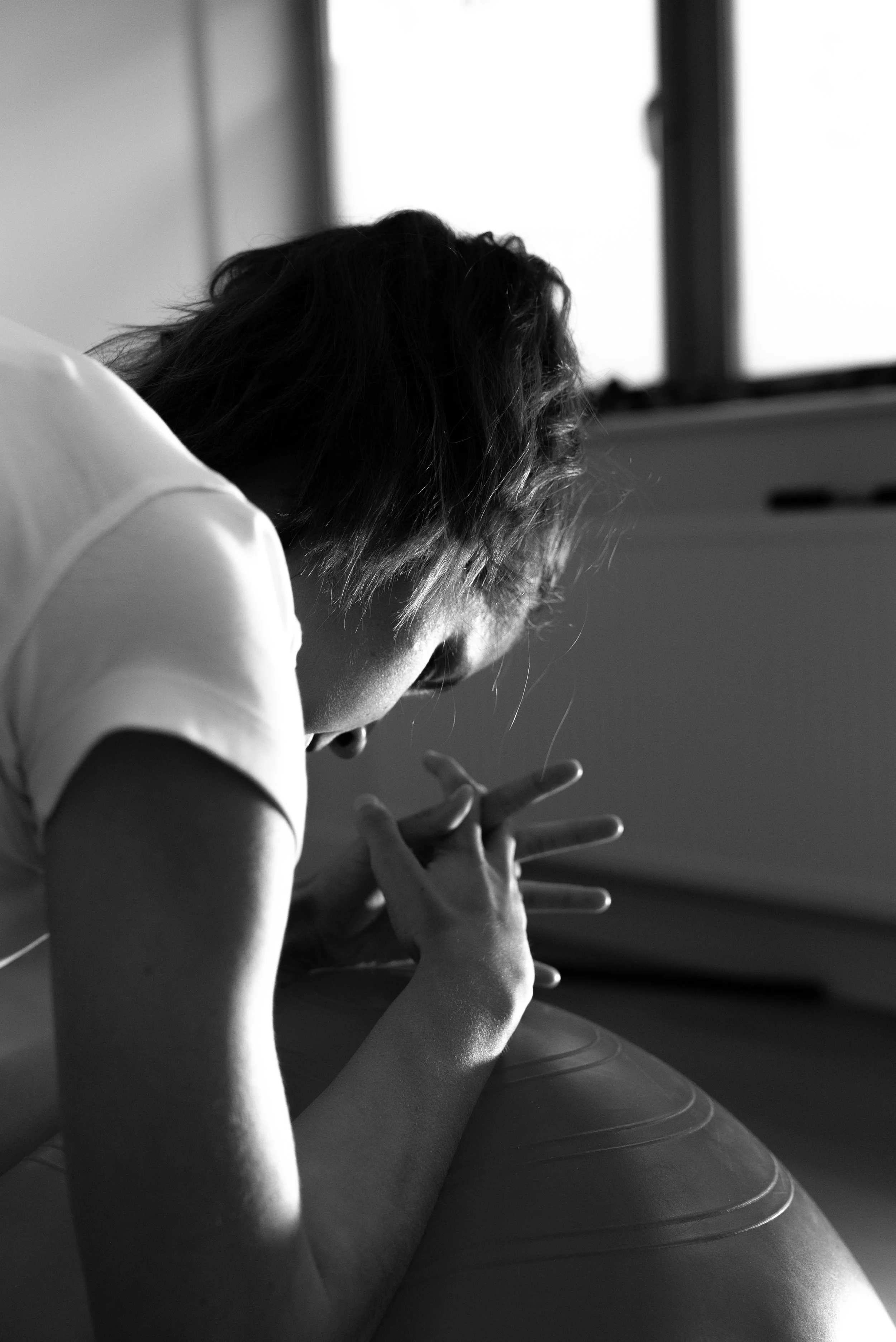 Zwart-wit foto van een persoon die op een grote fitnessbal ligt, met handen in een meditatie- of ontspanningshouding verbonden.