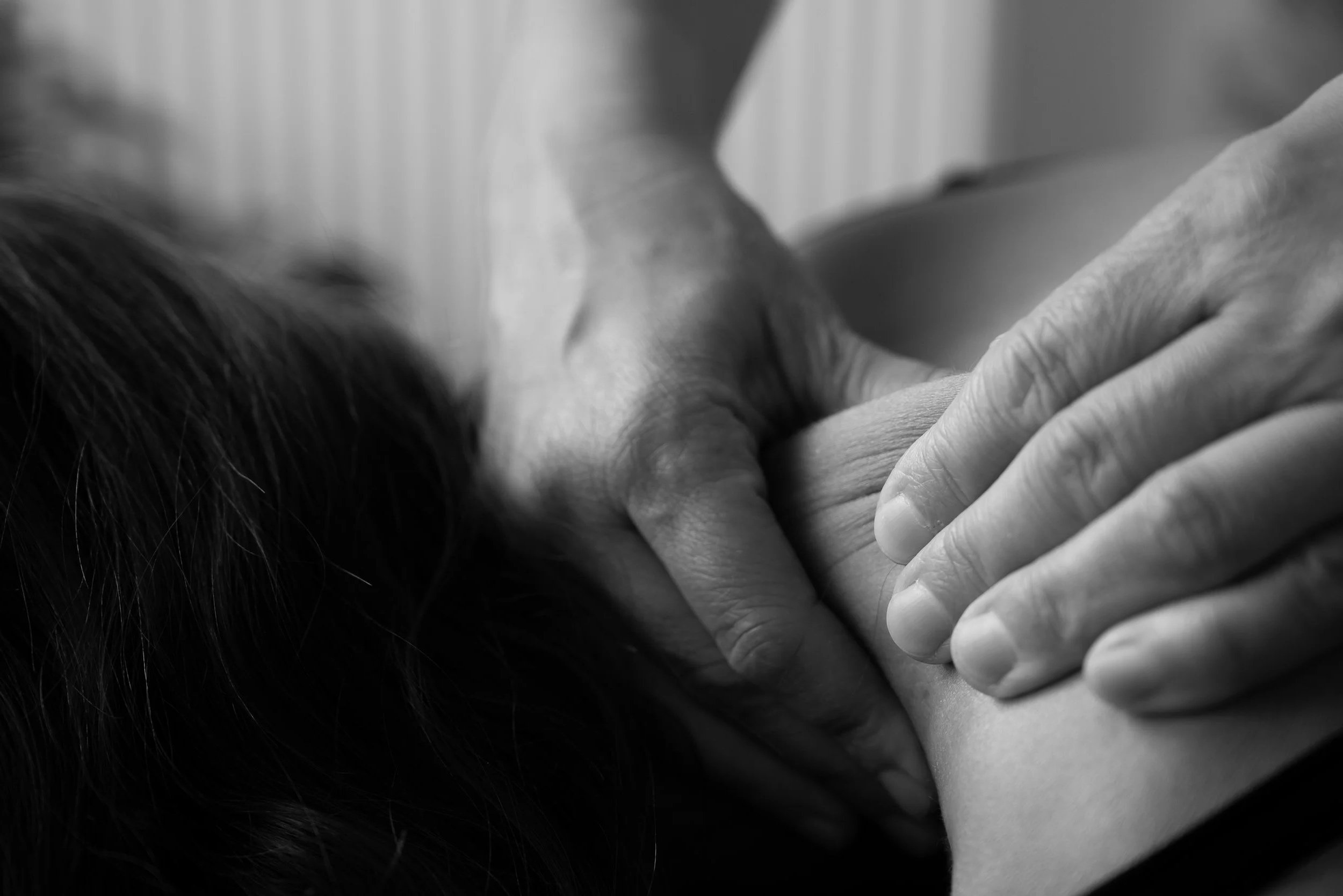 Zwarte en witte foto van een persoon die een intense kniebhukking krijgt van een therapeut of masseur, die haar nek en schouders masseren.