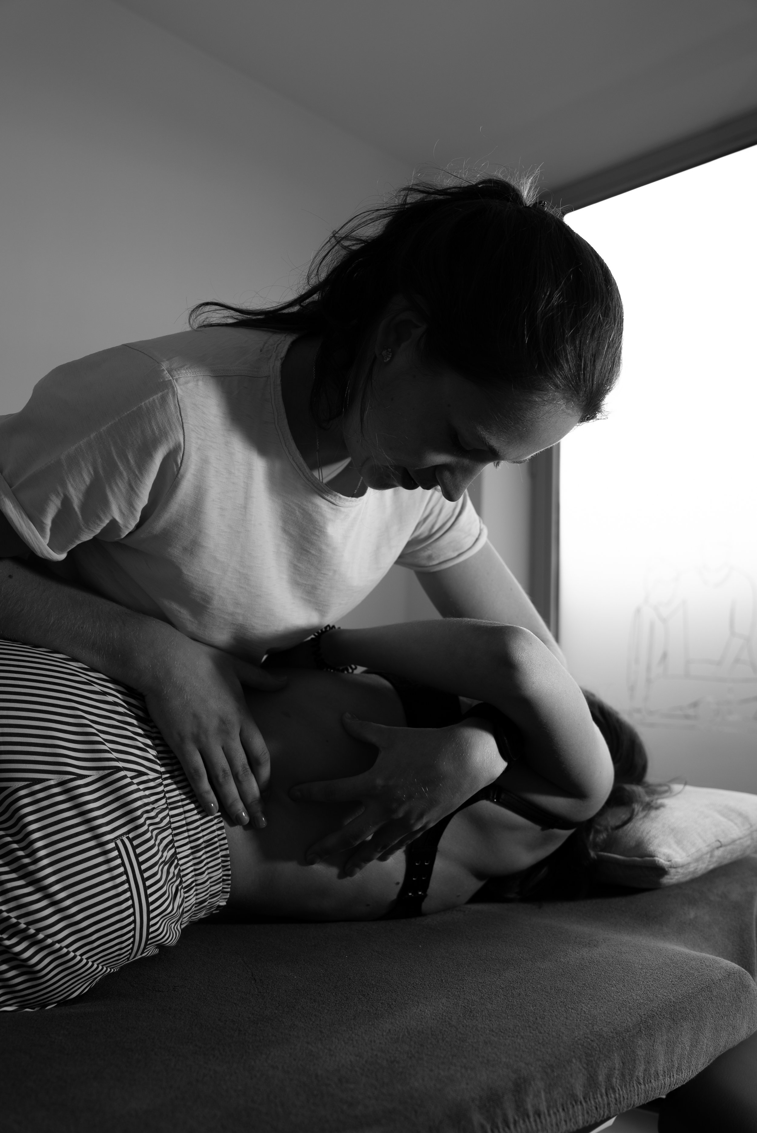 Een persoon geeft hedendaagse massage aan een andere persoon op een bed, in zwart-wit.