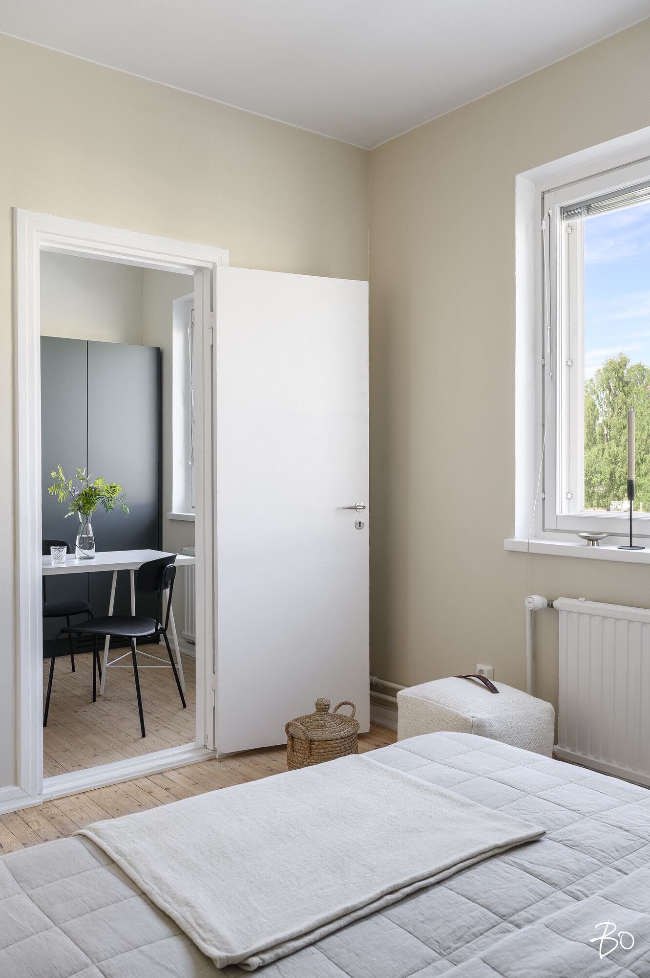 Yksi makuuhuone, jossa on sänky ja ikkunasta näkyy puita ja taivasta, sekä pieni avokeittiö, jossa on pöytä ja tuoleja.