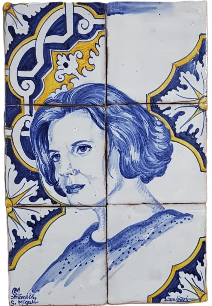 A painted portrait of a woman with short hair, painted in shades of blue and white, on tiled ceramic pieces, with decorative yellow and dark blue patterns around her head.