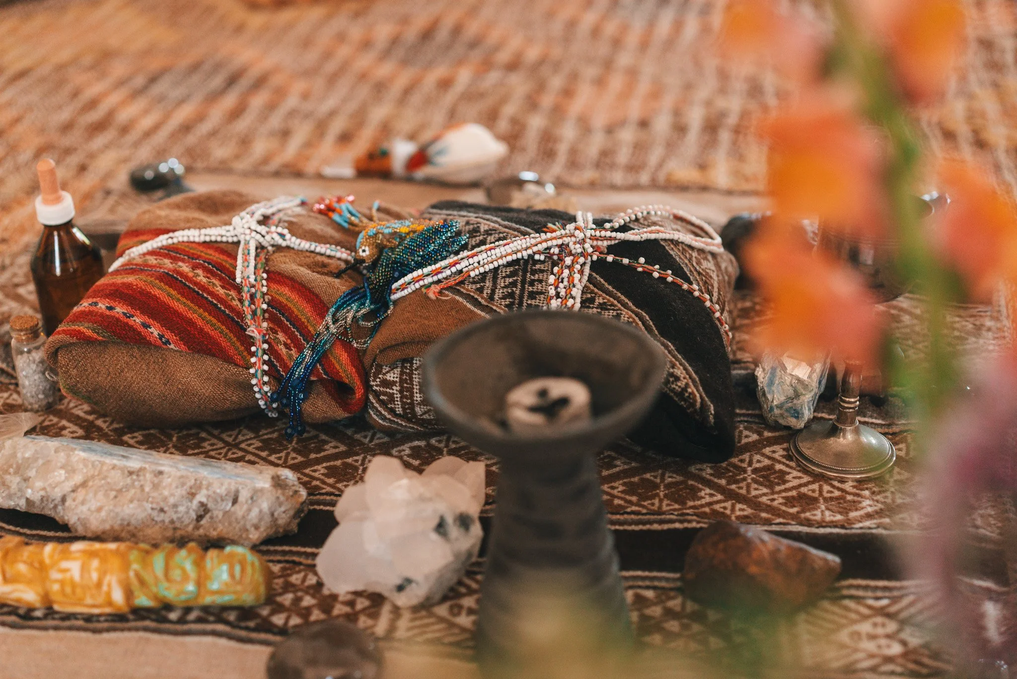 Objetos diversos sobre un tapete, incluyendo telas, collares, piedras, frascos y una vela, en un entorno oriental.