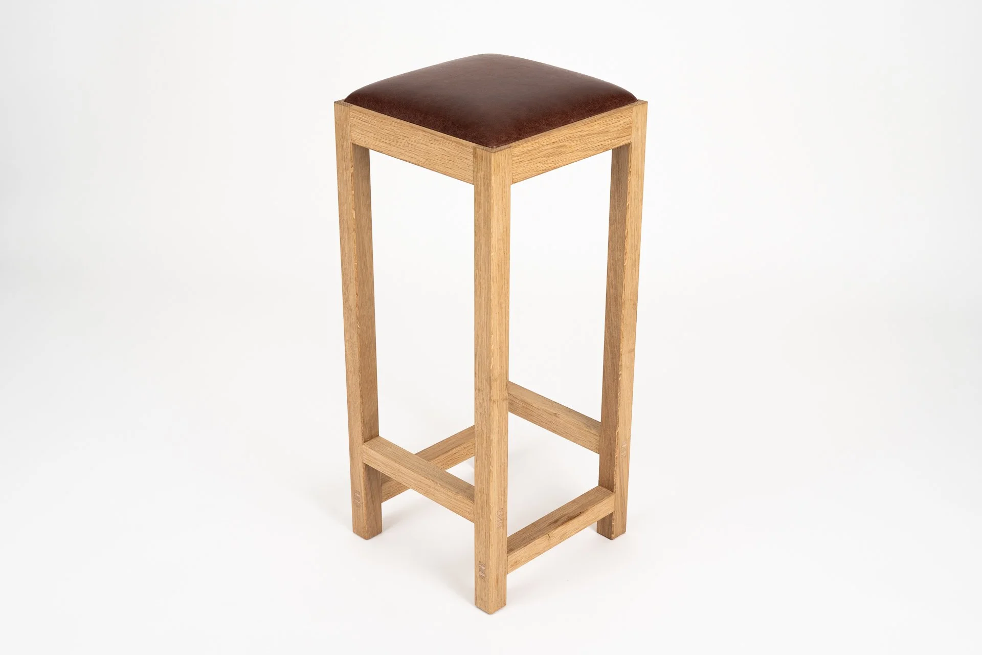 A wooden barstool with a cushioned brown leather seat, placed against a white background.