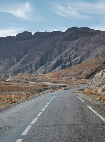 Eine Straße in einer wüstenähnlichen Landschaft mit Bergen im Hintergrund unter einem blauen Himmel.