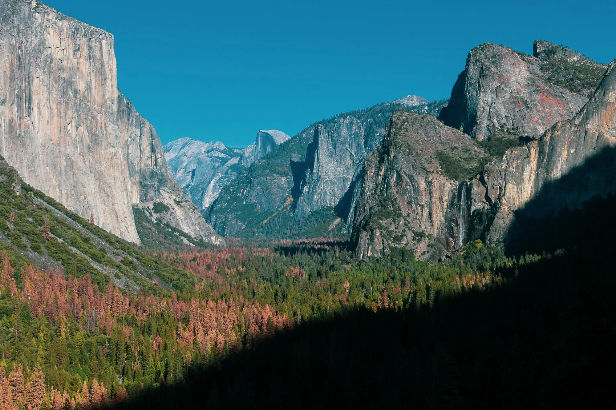 Berglandschaft mit hohen Felswänden, bewaldeten Tälern und klarem blauen Himmel