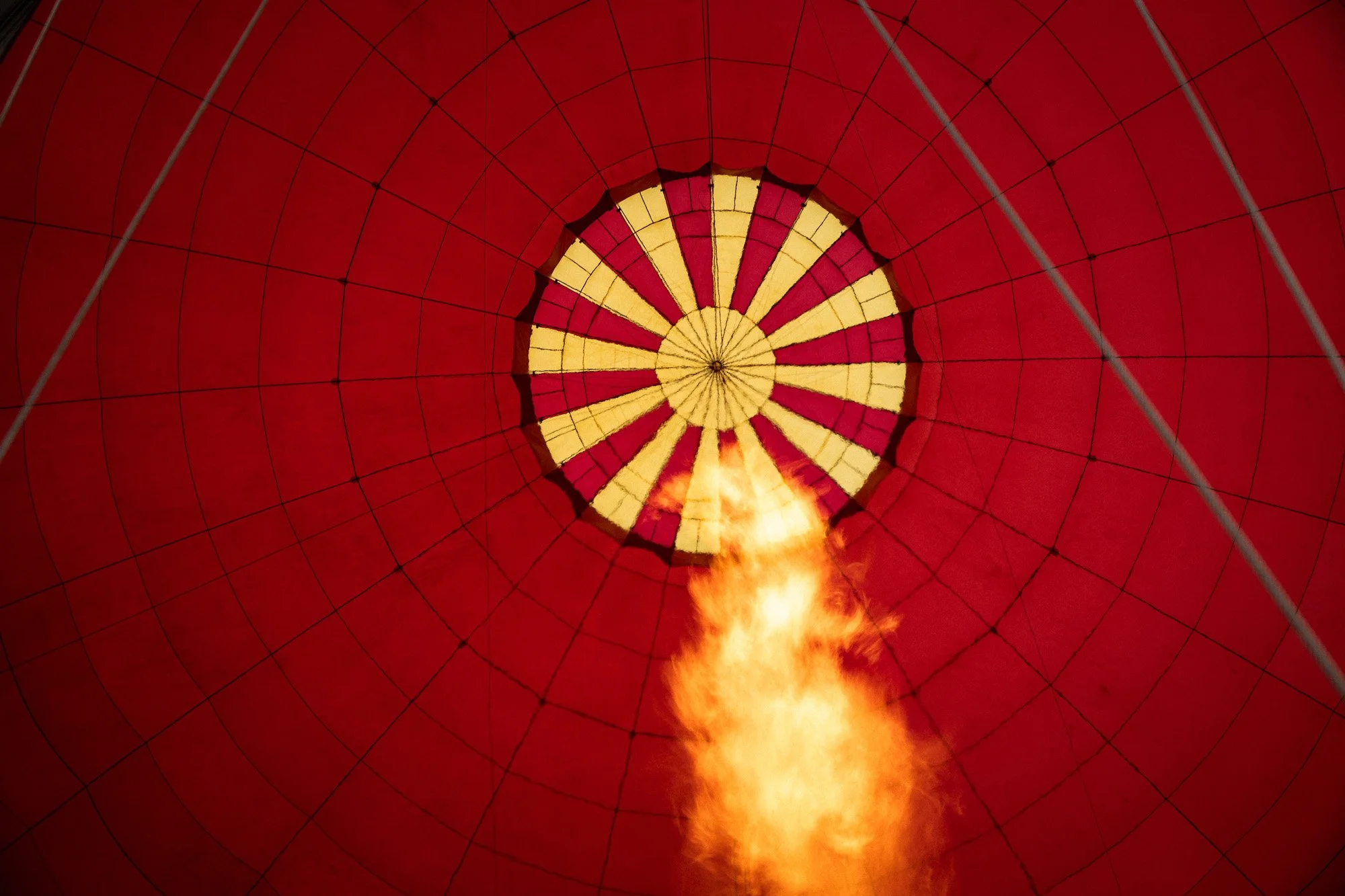 Innenansicht eines Heißluftballons, Blick nach oben, mit brennendem Gasbrenner, roter Ballonhülle mit gelben und roten Mustern