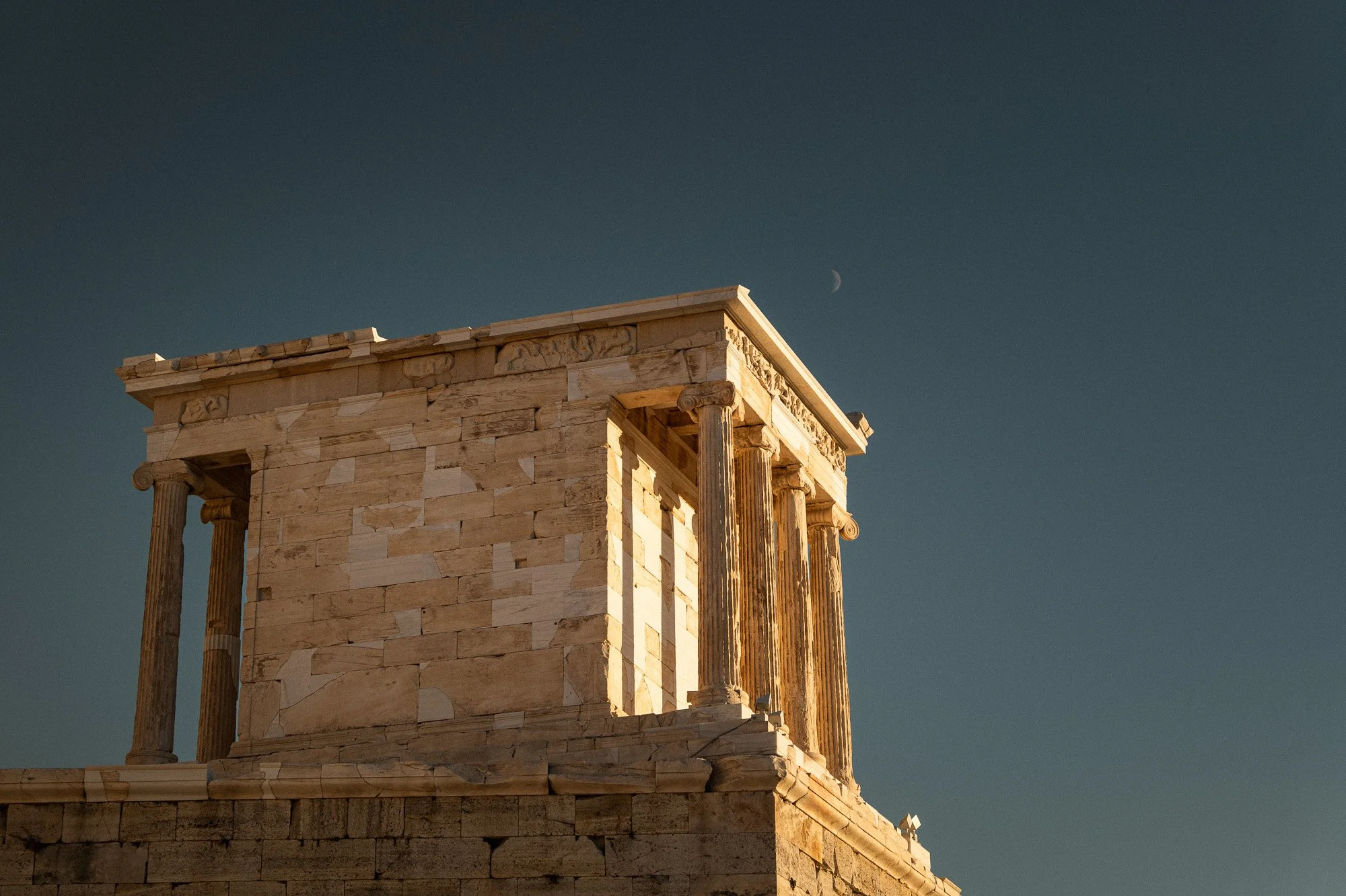 Antike griechische Tempelruine mit Säulen vor klarem Himmel bei Sonnenuntergang, Mond sichtbar