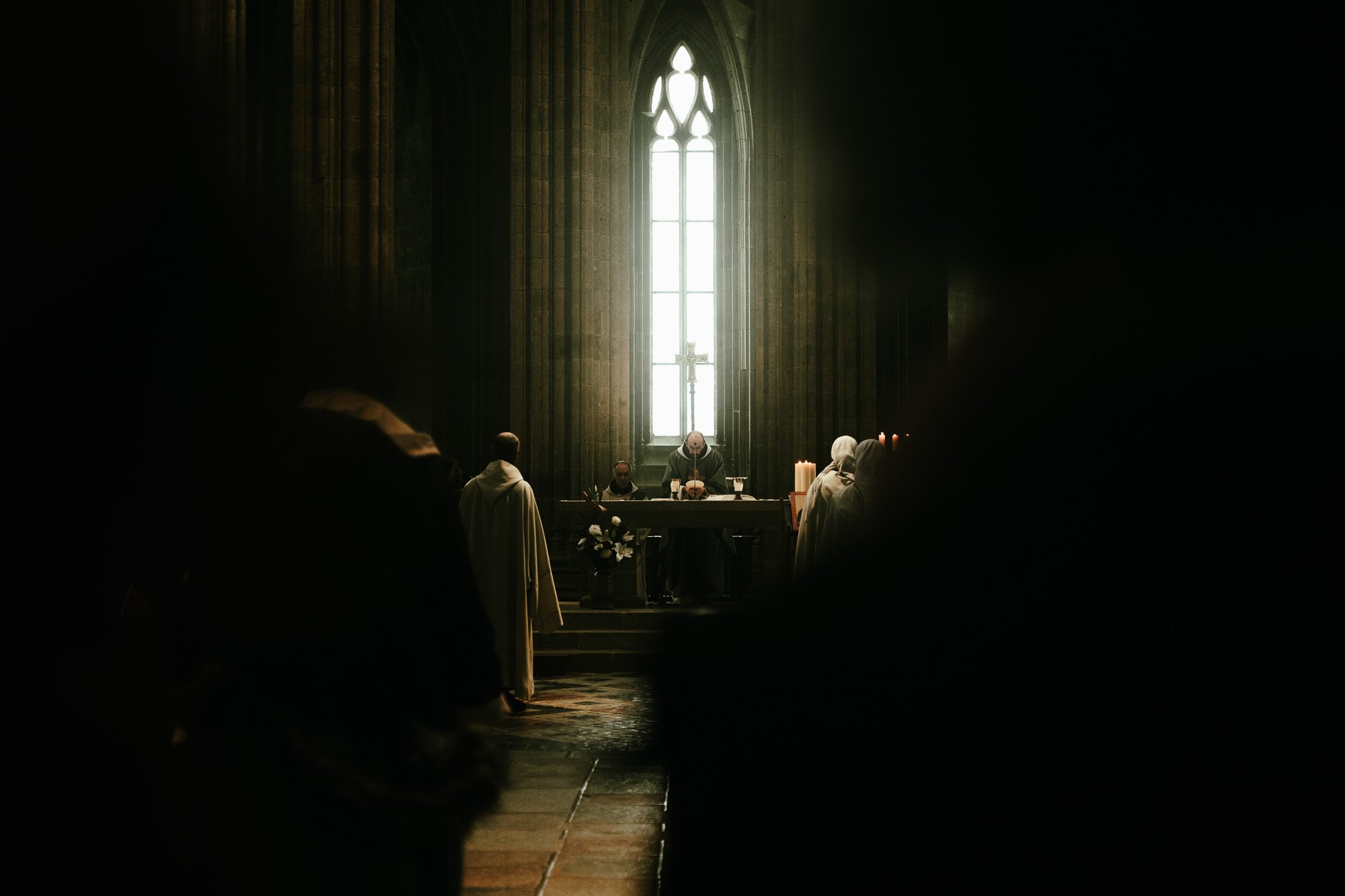 Innenraum einer Kirche während eines Gottesdienstes, mit Blick auf den Altar, beleuchtet durch ein großes Fenster, mit mehreren anwesenden Gläubigen.