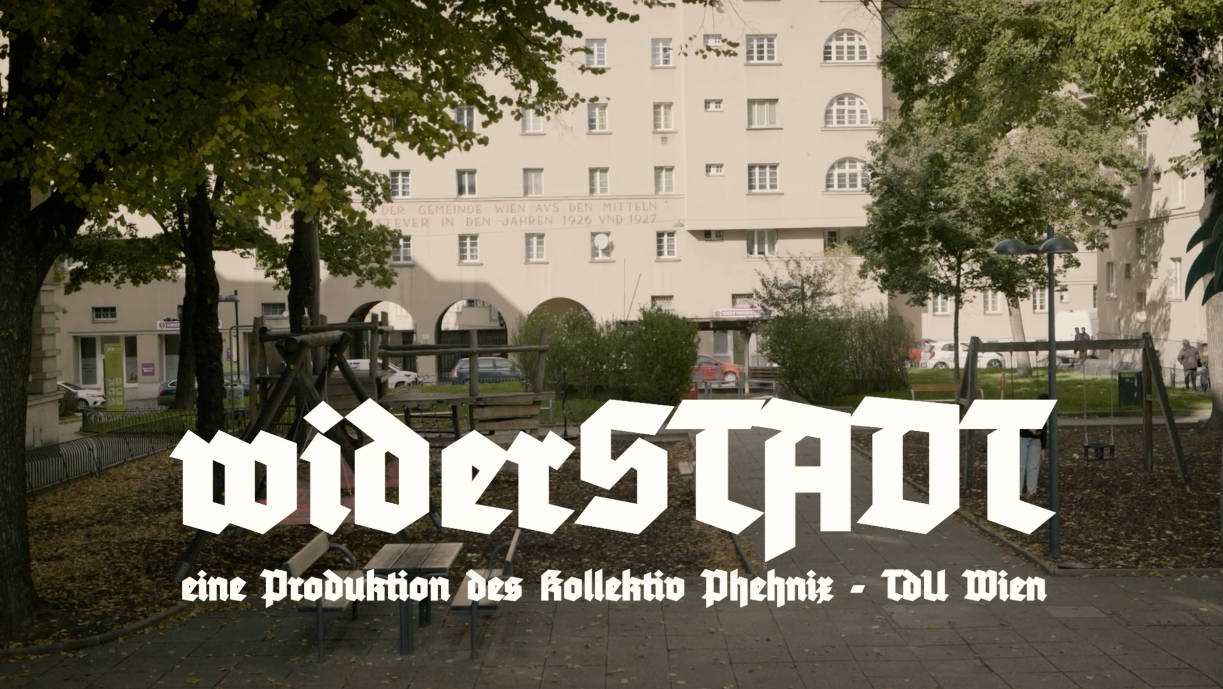 Ein Kinderspielplatz im Park mit Bäumen, Spielgeräten und einer Sitzbank. Im Hintergrund ein mehrstöckiges helles Gebäude. Über dem Bild schwebender Text sagt 'MIDÖSTAN' und darunter 'eine Produktion des kollektivo Pheenix - TDU Wien'.