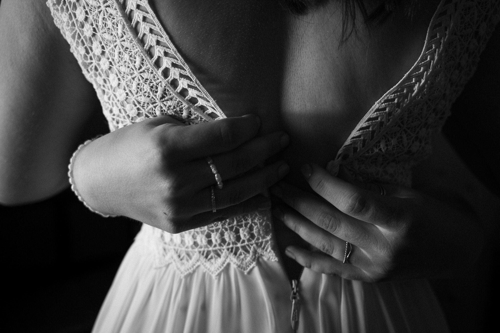 Nahaufnahme einer Frau in einem Kleid mit Stickerei, die ihre Hände auf die Brust legt, trägert Ringe und eine Perlenarmband, schwarz-weiß Fotografie