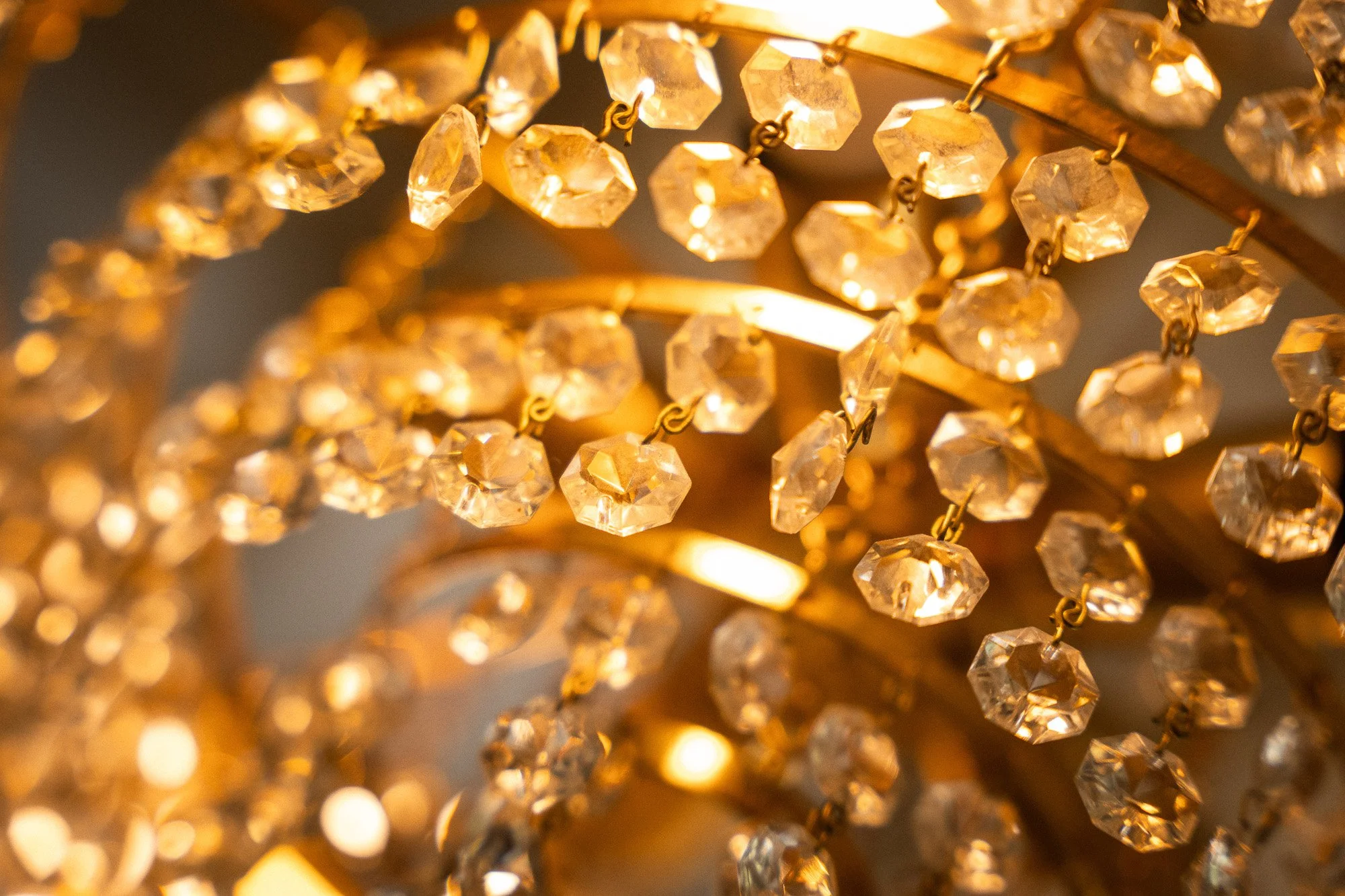 Nahaufnahme eines Kronleuchters mit goldfarbenen Rahmen und vielen funkelnden Kristallglas-Details, die warmes Licht reflektieren.