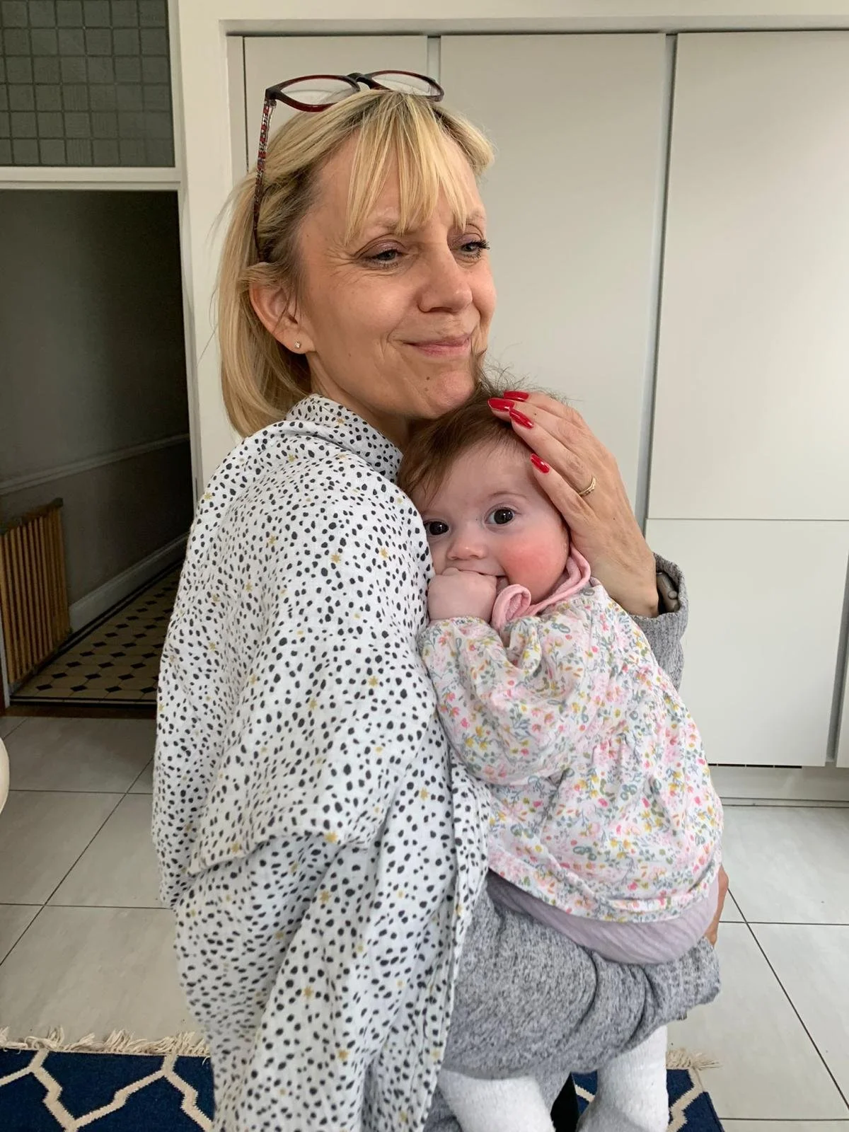 A man with glasses and styled dreadlocks working on a laptop at a desk, smiling.